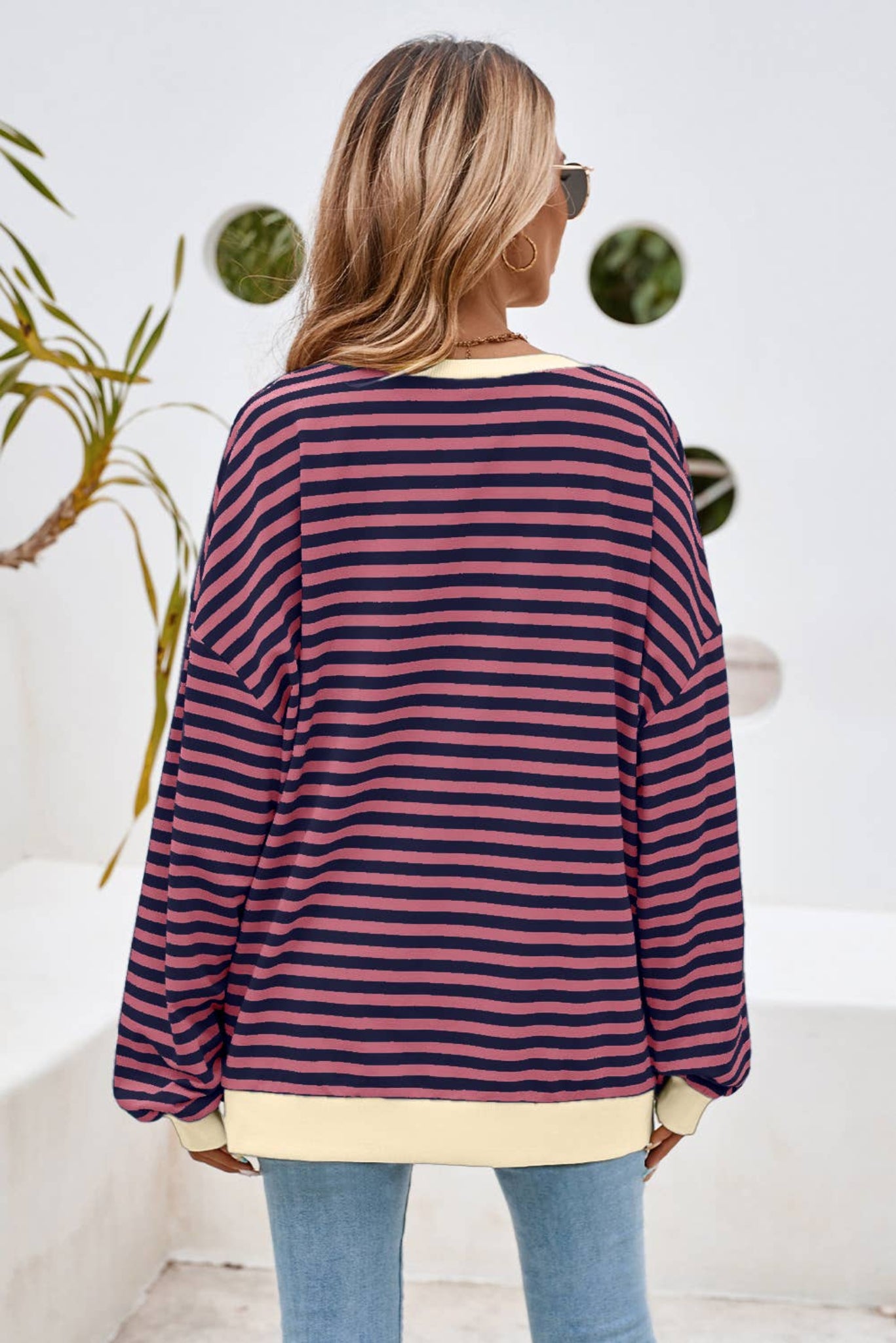 A woman wearing a striped oversized pullover sweatshirt in blue and yellow, paired with ripped jeans and sunglasses.