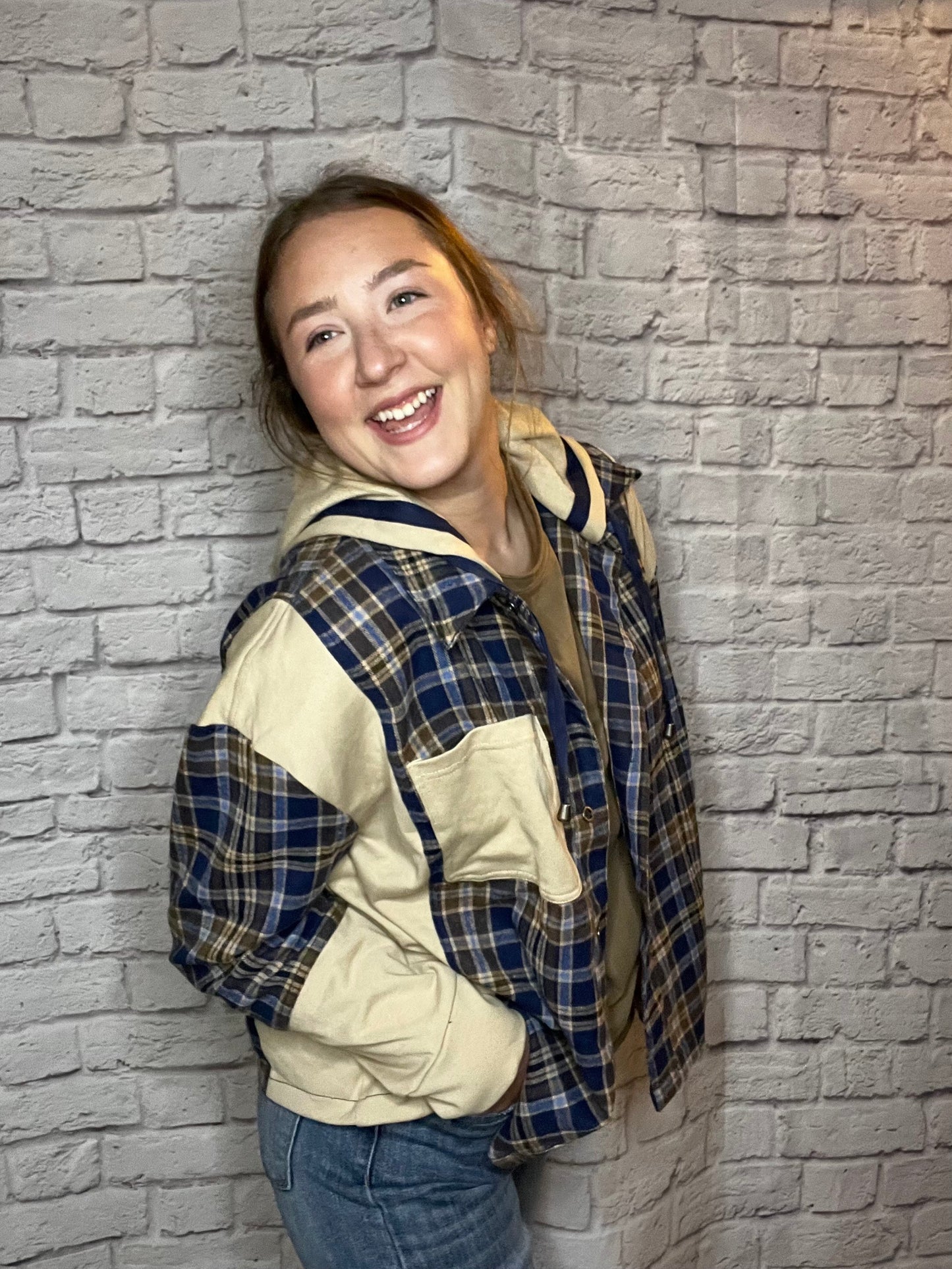 A woman wearing a blue, brown, and cream plaid shacket featuring cream contrast sleeves and large front pocket.