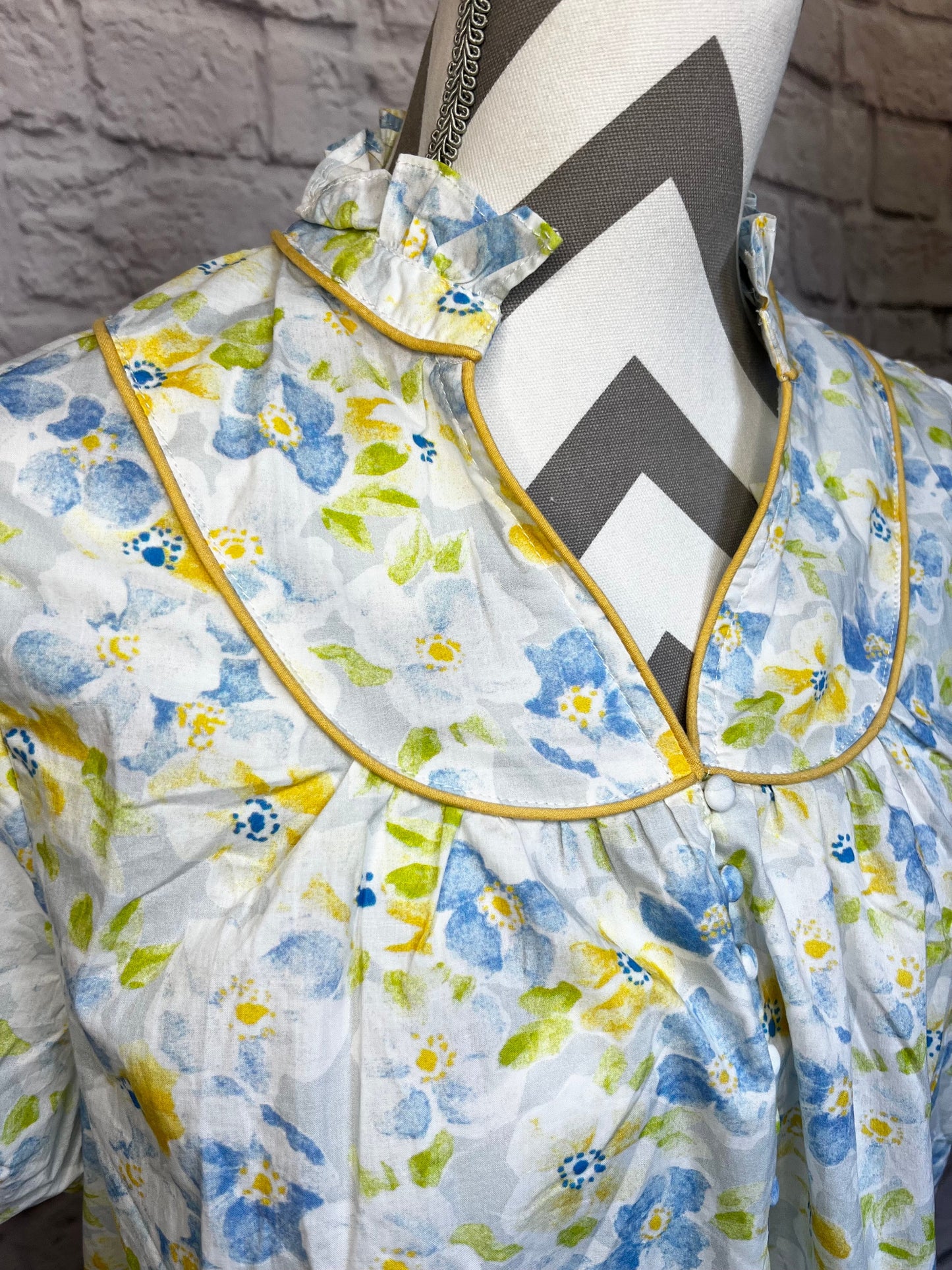 Floral-patterned dress with a large bow on a mannequin against a brick wall.