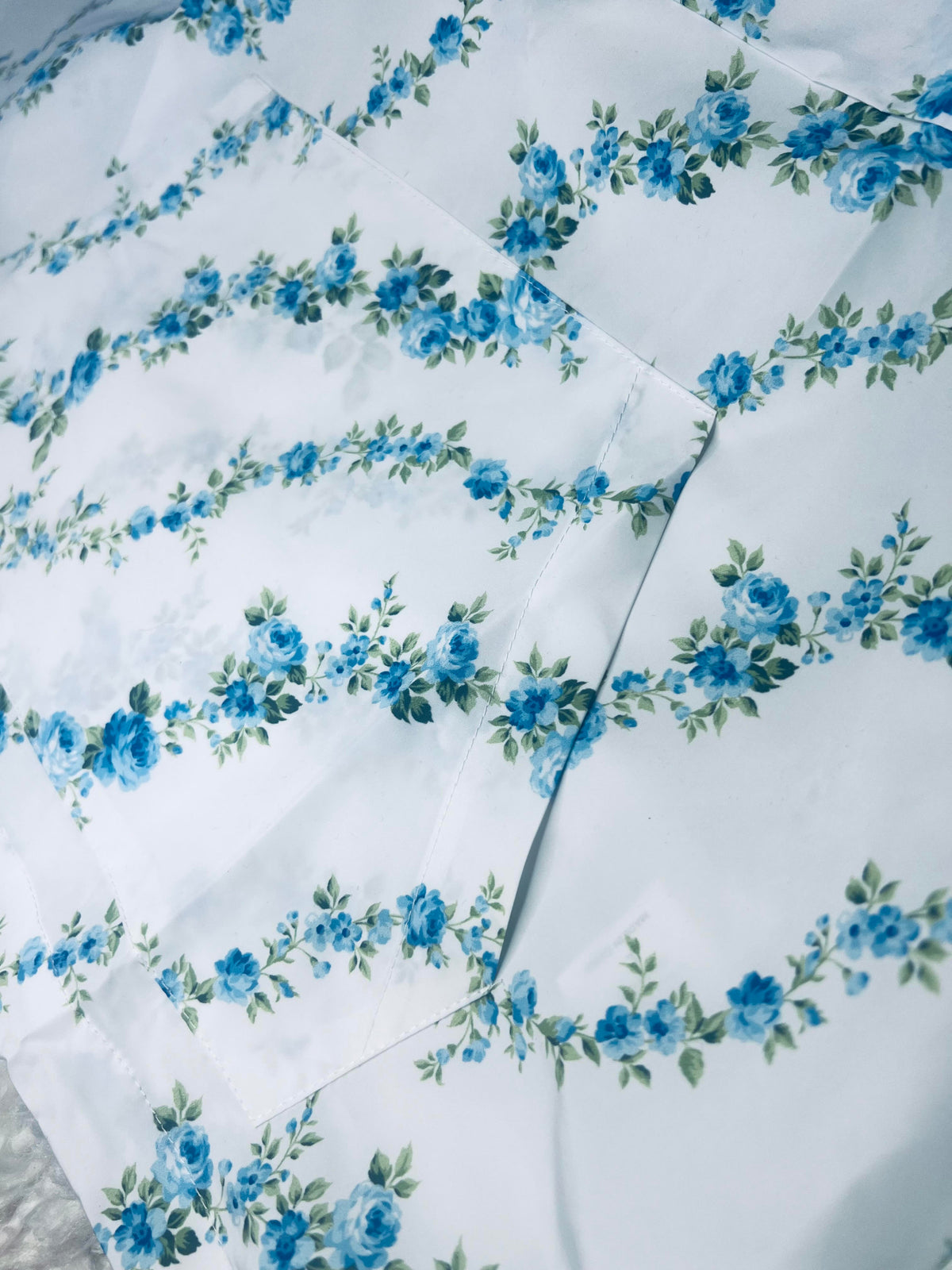 A light blue windbreaker with a floral pattern displayed on a mannequin against a brick wall backdrop.