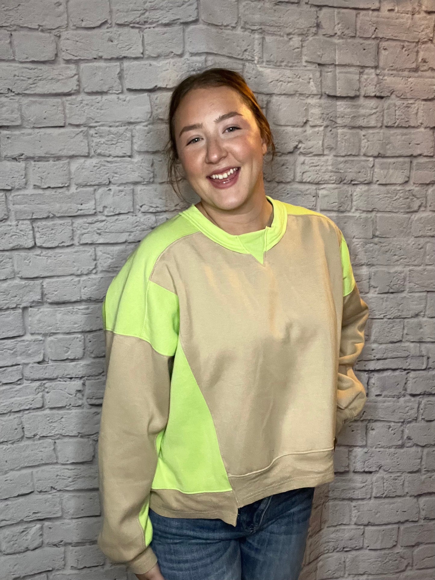 A woman wearing a casual sweatshirt with tan and neon yellow color-block sleeves and accents.