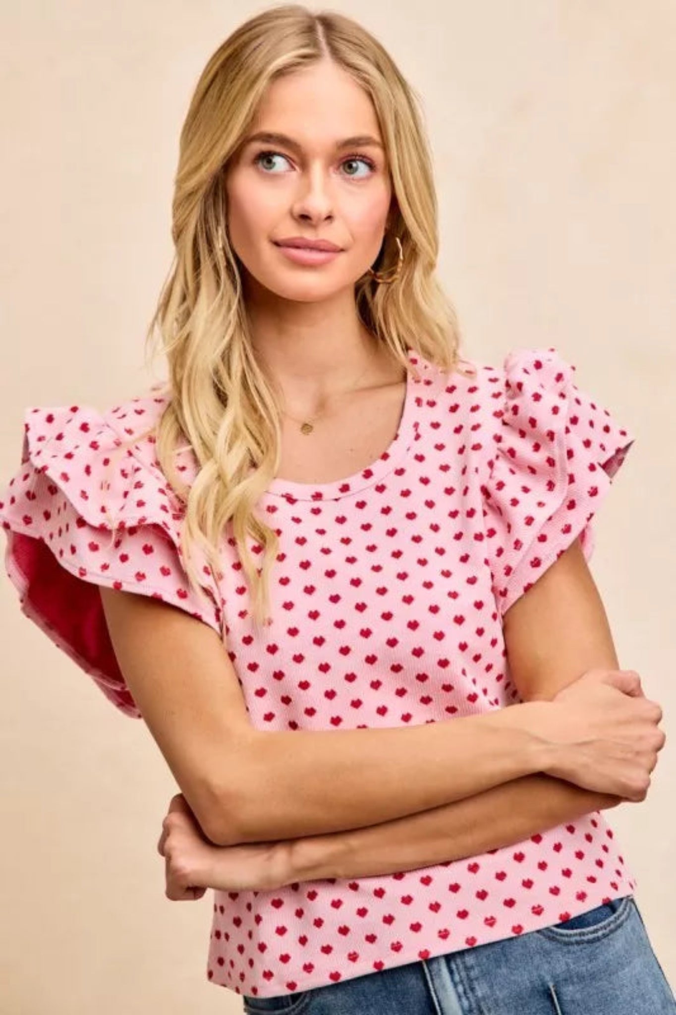 Pink heart print ruffle sleeve knit top with flutter shoulders and fitted silhouette on a model against a neutral background