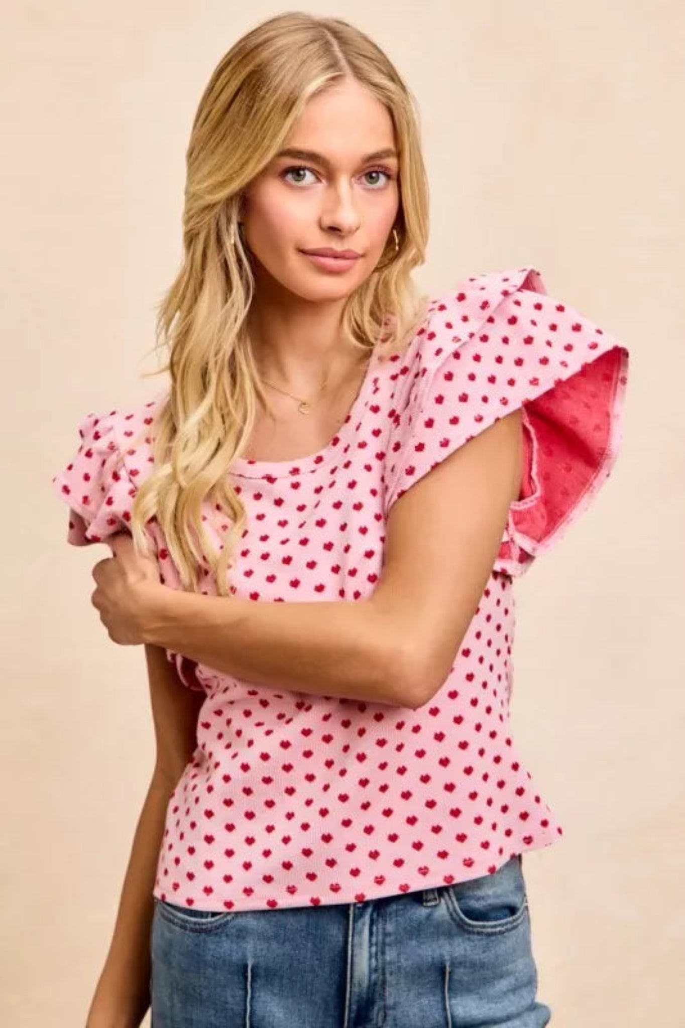 Pink heart print ruffle sleeve knit top with flutter shoulders and fitted silhouette on a model against a neutral background