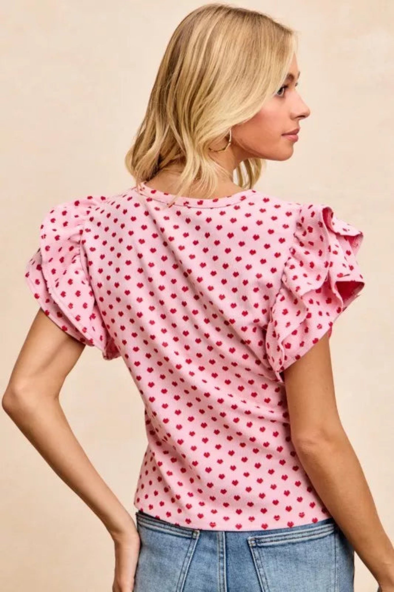 Pink heart print ruffle sleeve knit top with flutter shoulders and fitted silhouette on a model against a neutral background