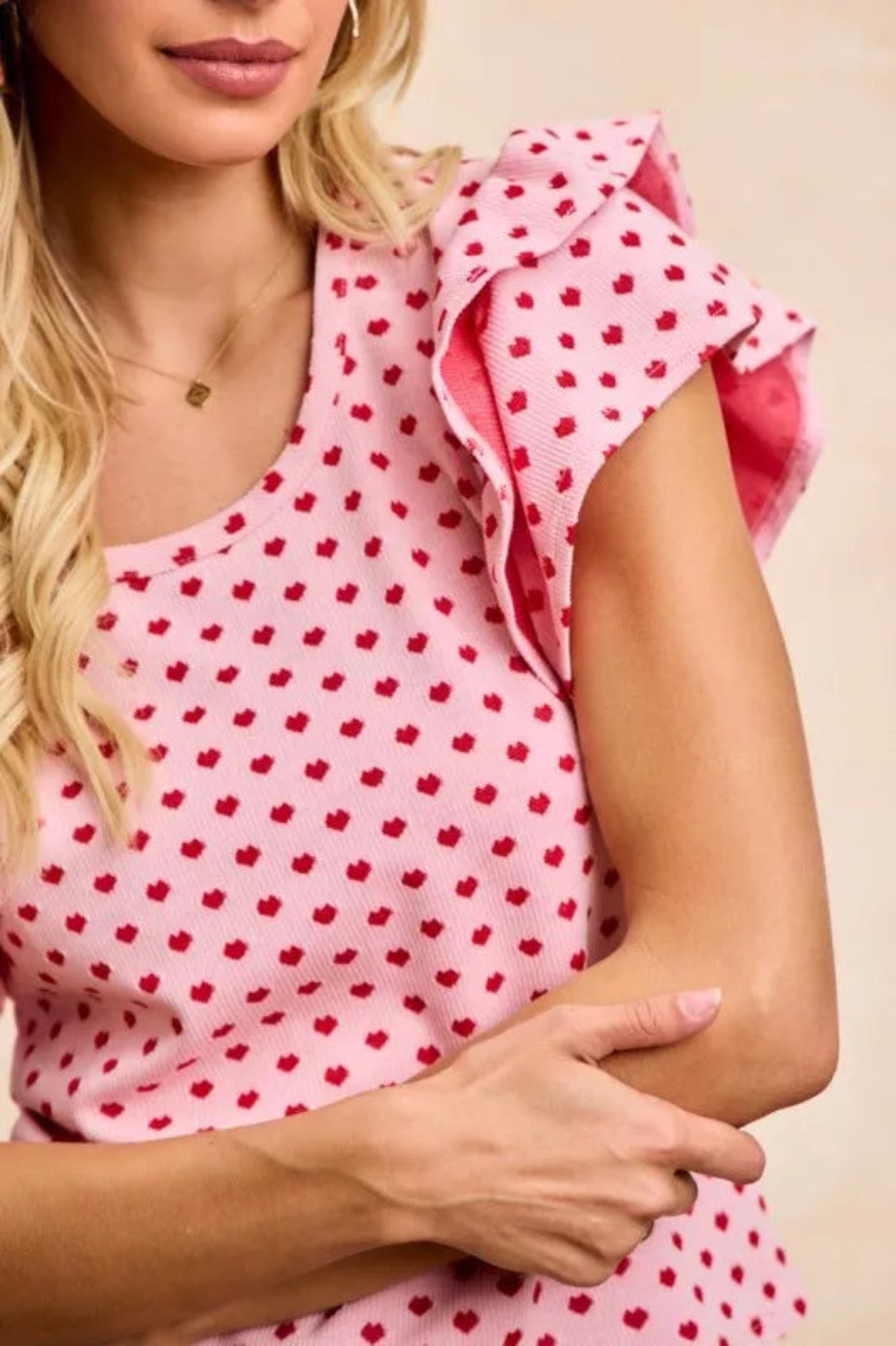 Pink heart print ruffle sleeve knit top with flutter shoulders and fitted silhouette on a model against a neutral background