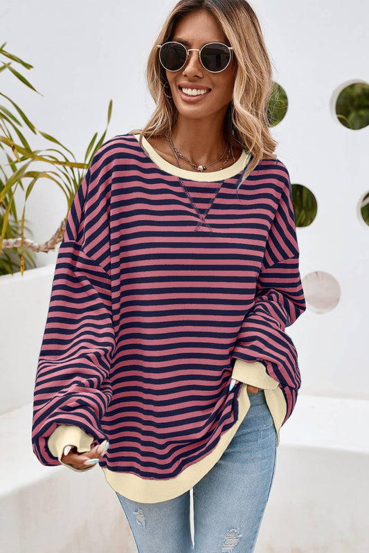 A woman wearing a striped oversized pullover sweatshirt in blue and yellow, paired with ripped jeans and sunglasses.