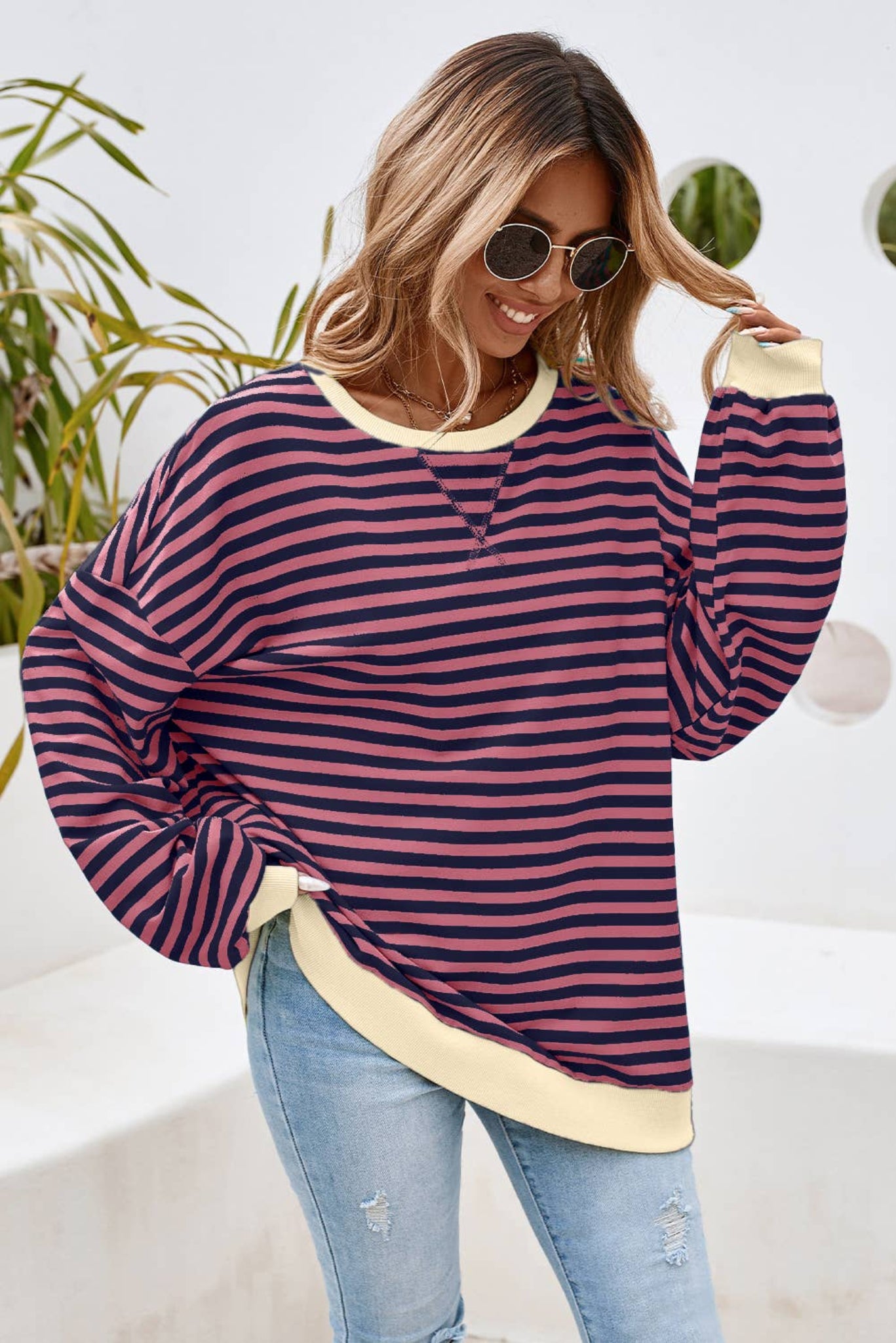 A woman wearing a striped oversized pullover sweatshirt in blue and yellow, paired with ripped jeans and sunglasses.