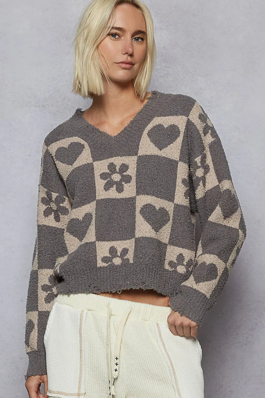 Gray checker knit sweater with heart and floral pattern, v-neckline, and long sleeves on a model against a textured background