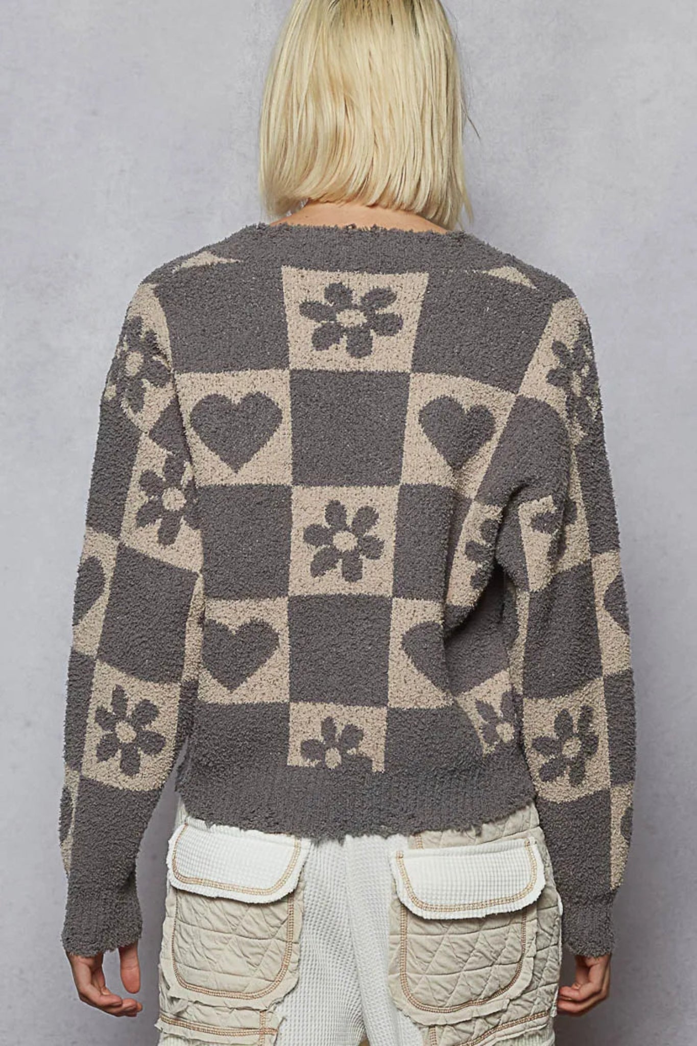 Gray checker knit sweater with heart and floral pattern, v-neckline, and long sleeves on a model against a textured background