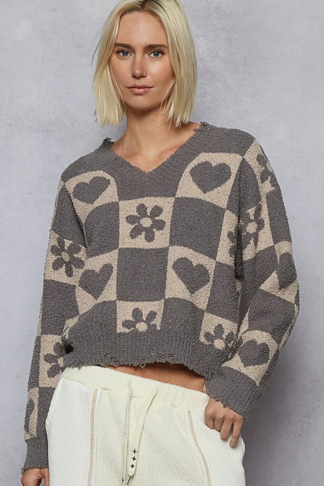 Gray checker knit sweater with heart and floral pattern, v-neckline, and long sleeves on a model against a textured background