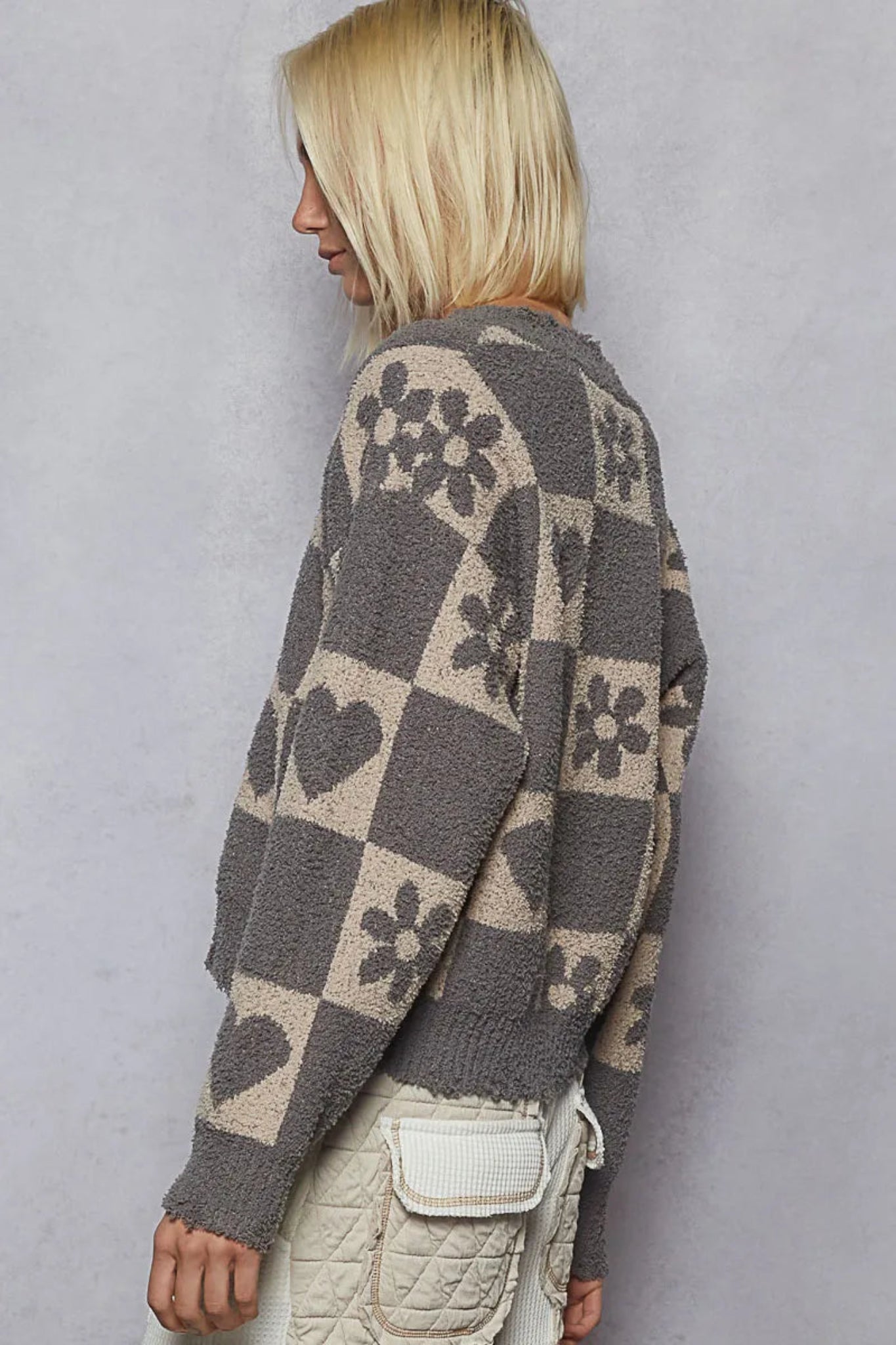 Gray checker knit sweater with heart and floral pattern, v-neckline, and long sleeves on a model against a textured background