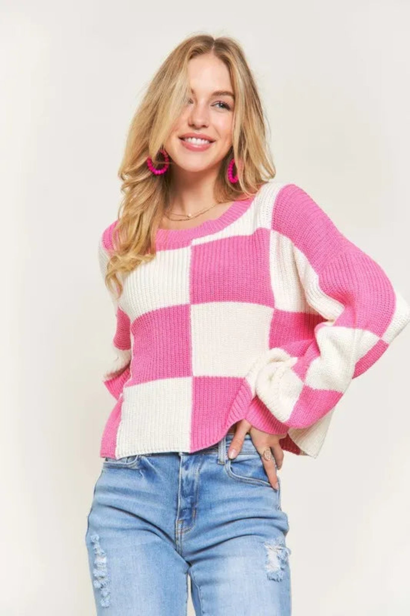 Pink and cream checker knit cropped sweater with crew neckline and long sleeves on a model against a light background