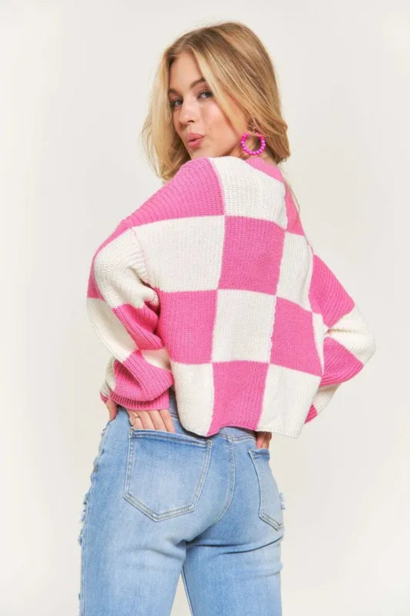 Pink and cream checker knit cropped sweater with crew neckline and long sleeves on a model against a light background