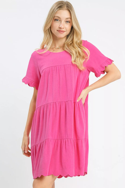 Peony pink tiered baby-doll dress with ruffle short sleeves and scalloped hem on a model against a white background