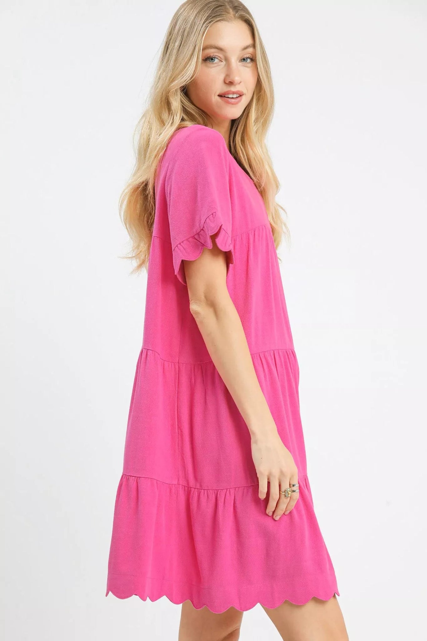 Peony pink tiered baby-doll dress with ruffle short sleeves and scalloped hem on a model against a white background