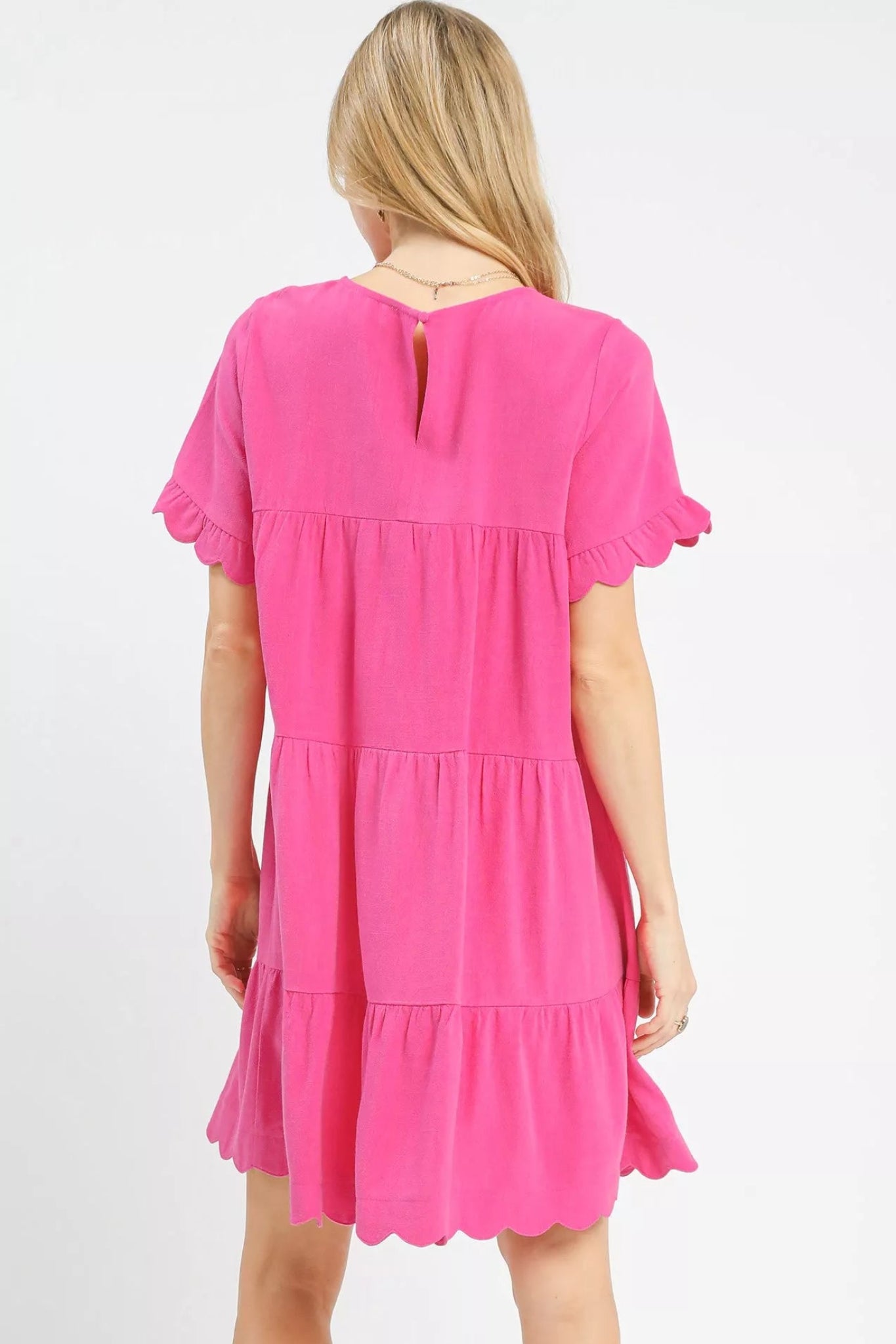 Peony pink tiered baby-doll dress with ruffle short sleeves and scalloped hem on a model against a white background