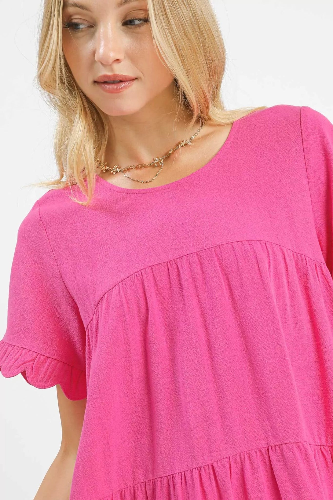 Peony pink tiered baby-doll dress with ruffle short sleeves and scalloped hem on a model against a white background