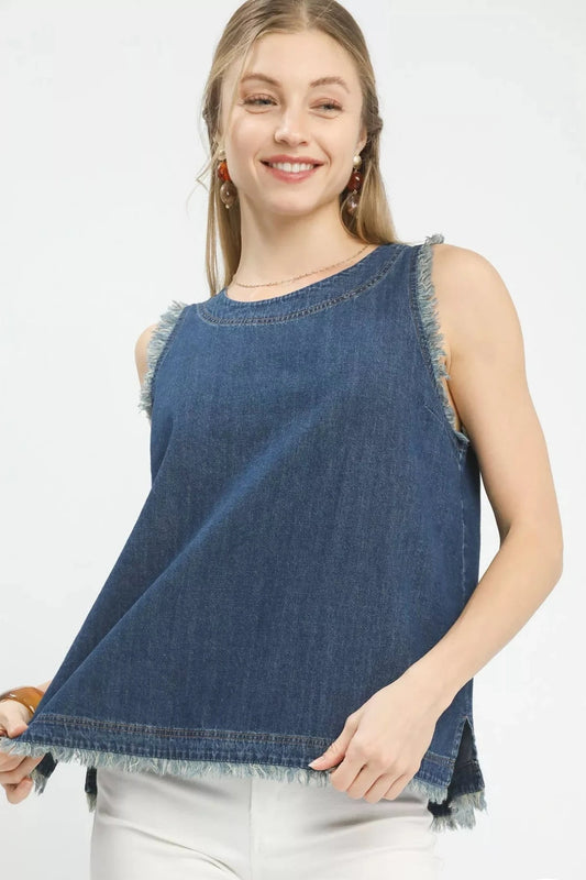 Woman wearing a sleeveless denim tank top with frayed trim edges and a relaxed fit, styled with white pants for a casual boutique look.