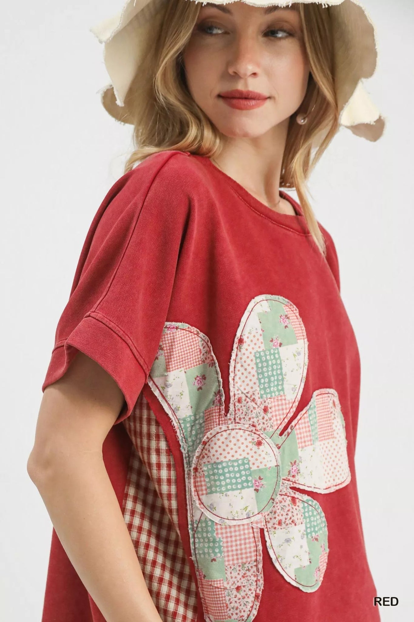Woman wearing a red short sleeve graphic tee with a patchwork floral design, styled with distressed denim shorts and a casual boho look.