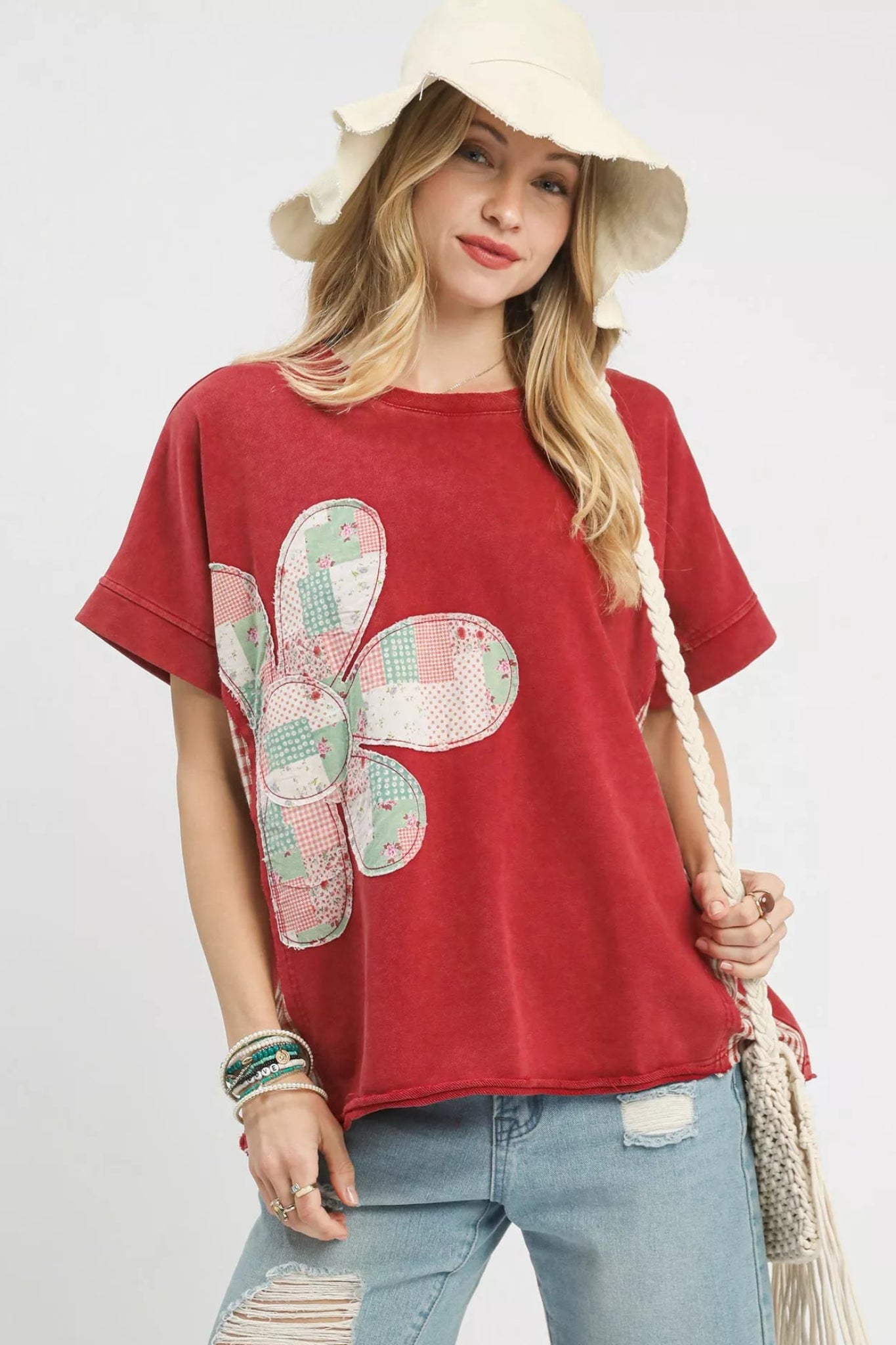 Woman wearing a red short sleeve graphic tee with a patchwork floral design, styled with distressed denim shorts and a casual boho look.