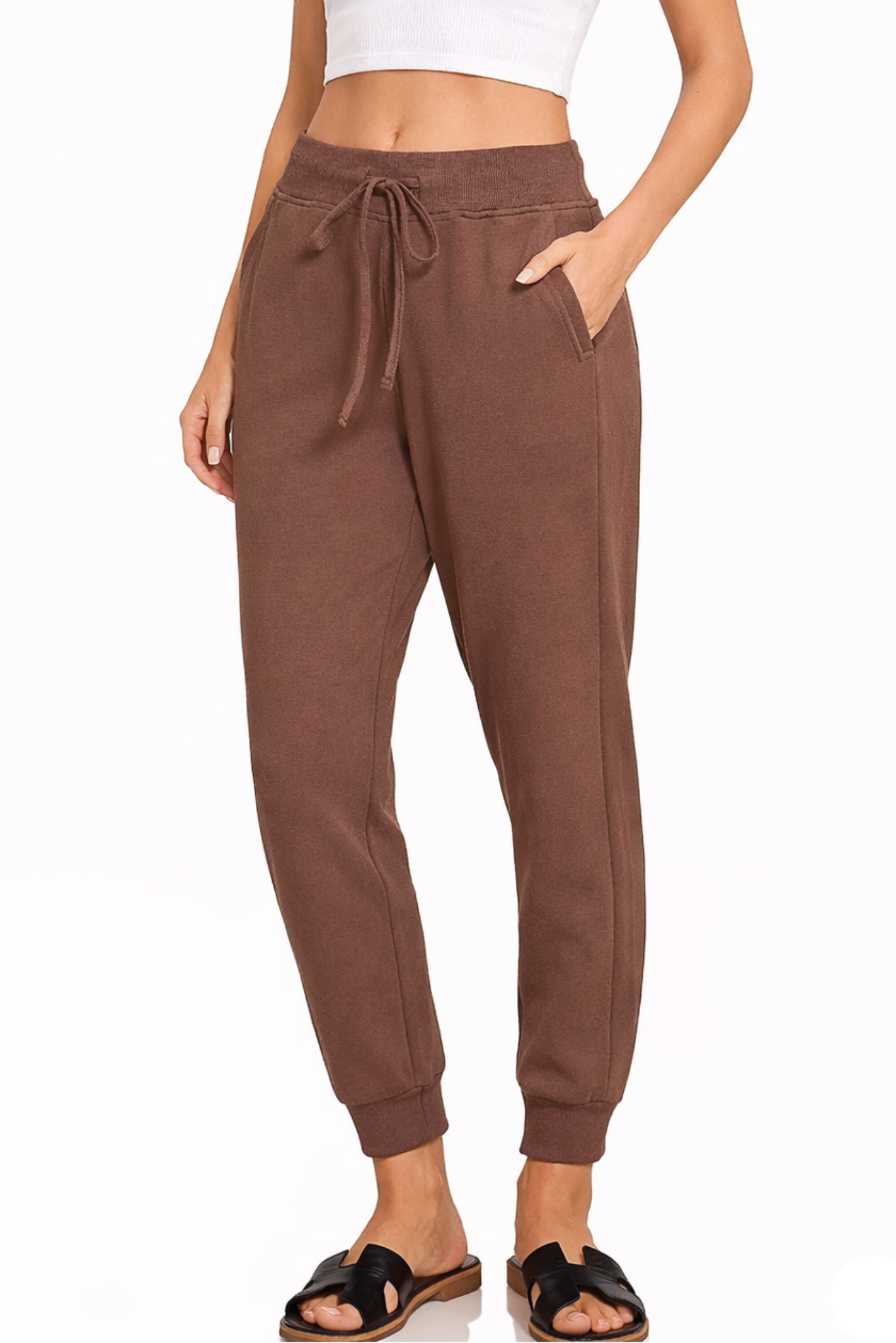 Model wearing brown jogger sweatpants with elastic waistband, drawstring tie, side pockets, and white cropped ribbed tank top.