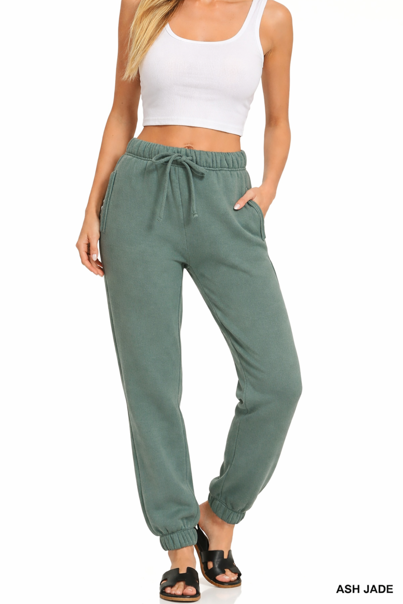 Model wearing ash jade jogger sweatpants with elastic waistband, drawstring tie, side pockets, and cropped white tank top.