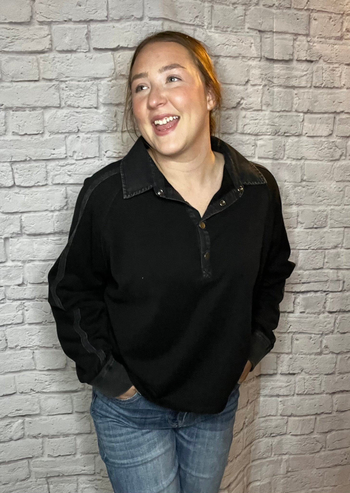 A woman wearing a black pullover with a snap-button collar and subtle seam details on the sleeves.