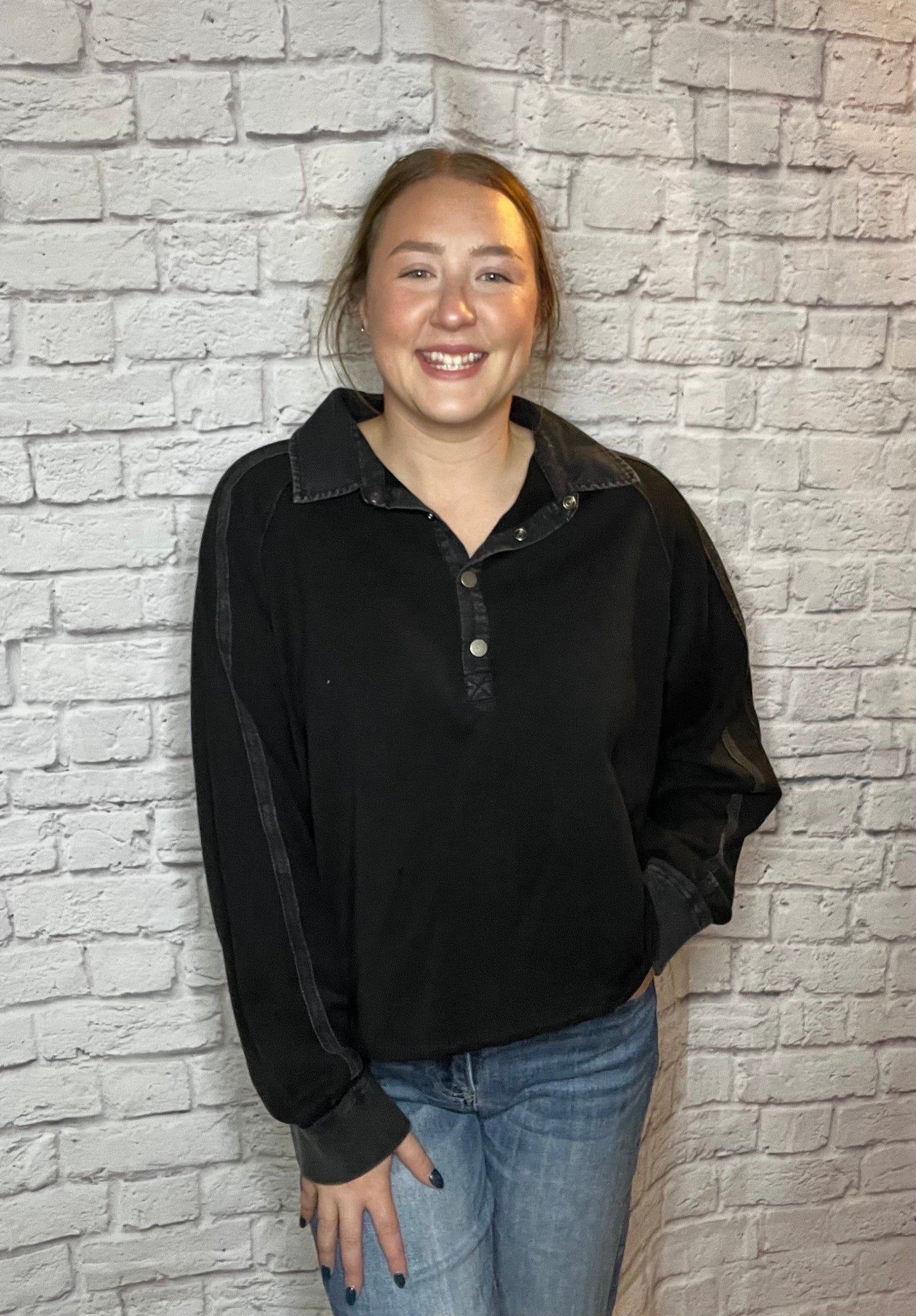 A woman wearing a black pullover with a snap-button collar and subtle seam details on the sleeves.