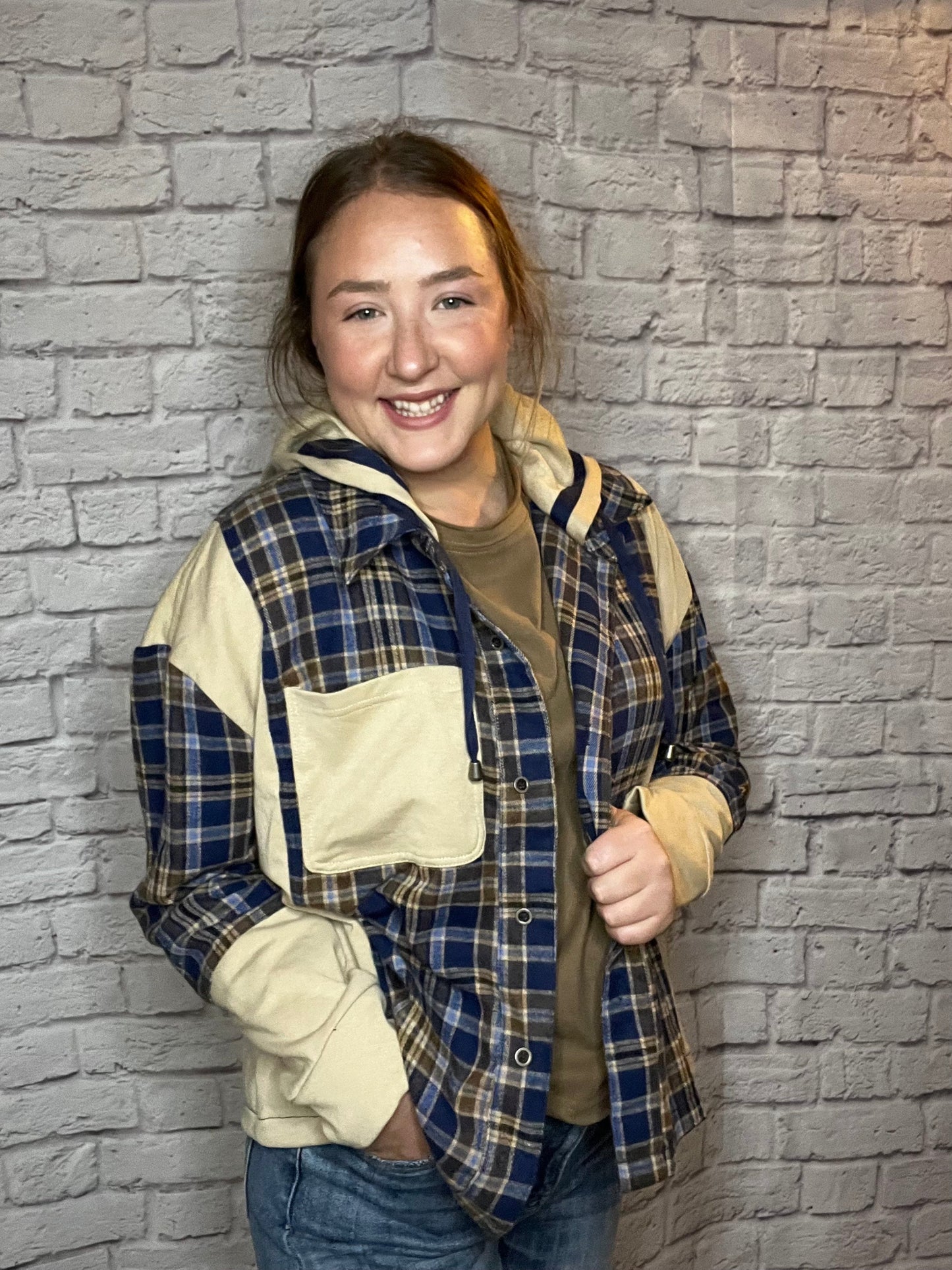 A woman wearing a blue, brown, and cream plaid shacket featuring cream contrast sleeves and large front pocket.