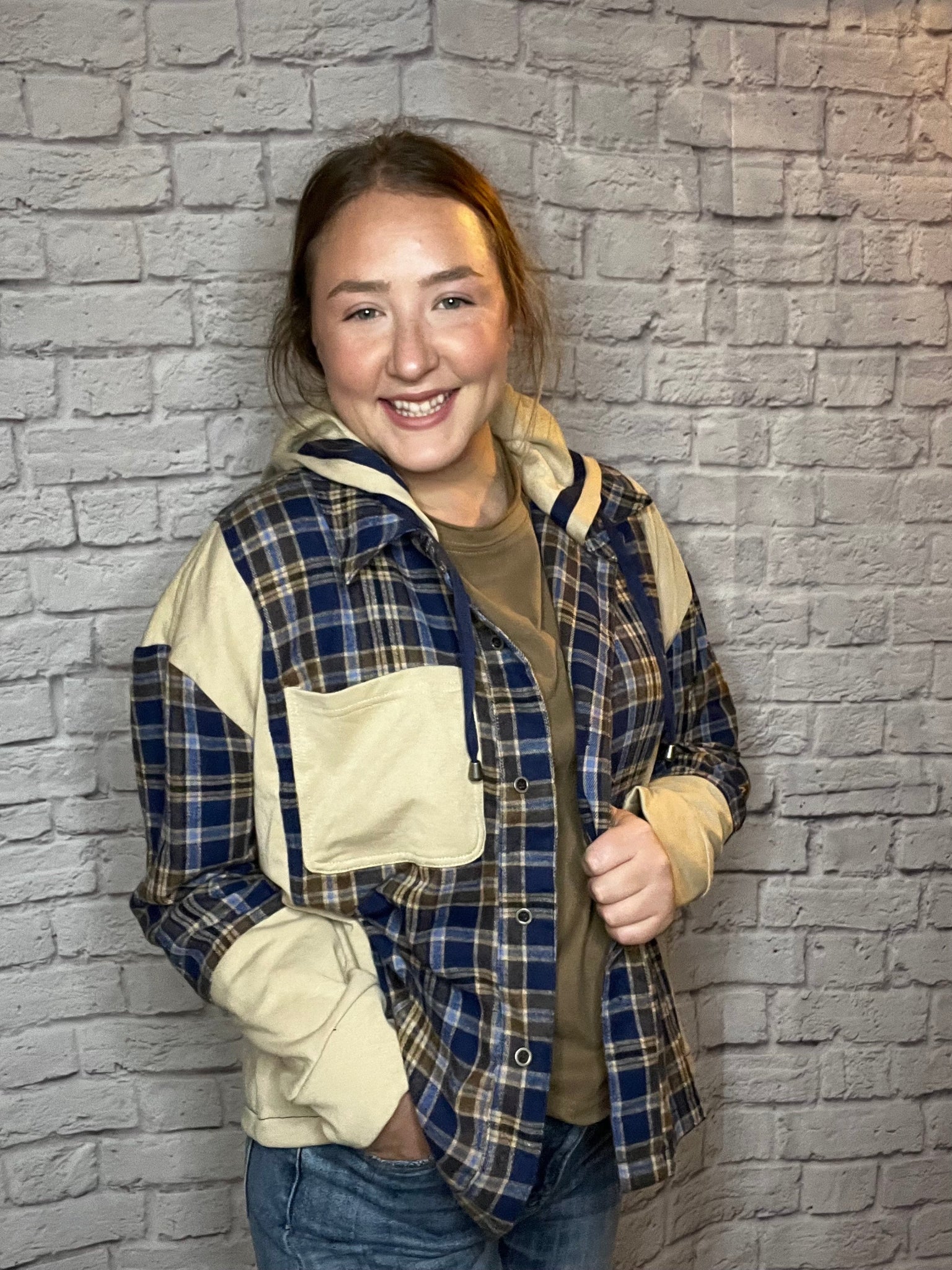 A woman wearing a blue, brown, and cream plaid shacket featuring cream contrast sleeves and large front pocket.