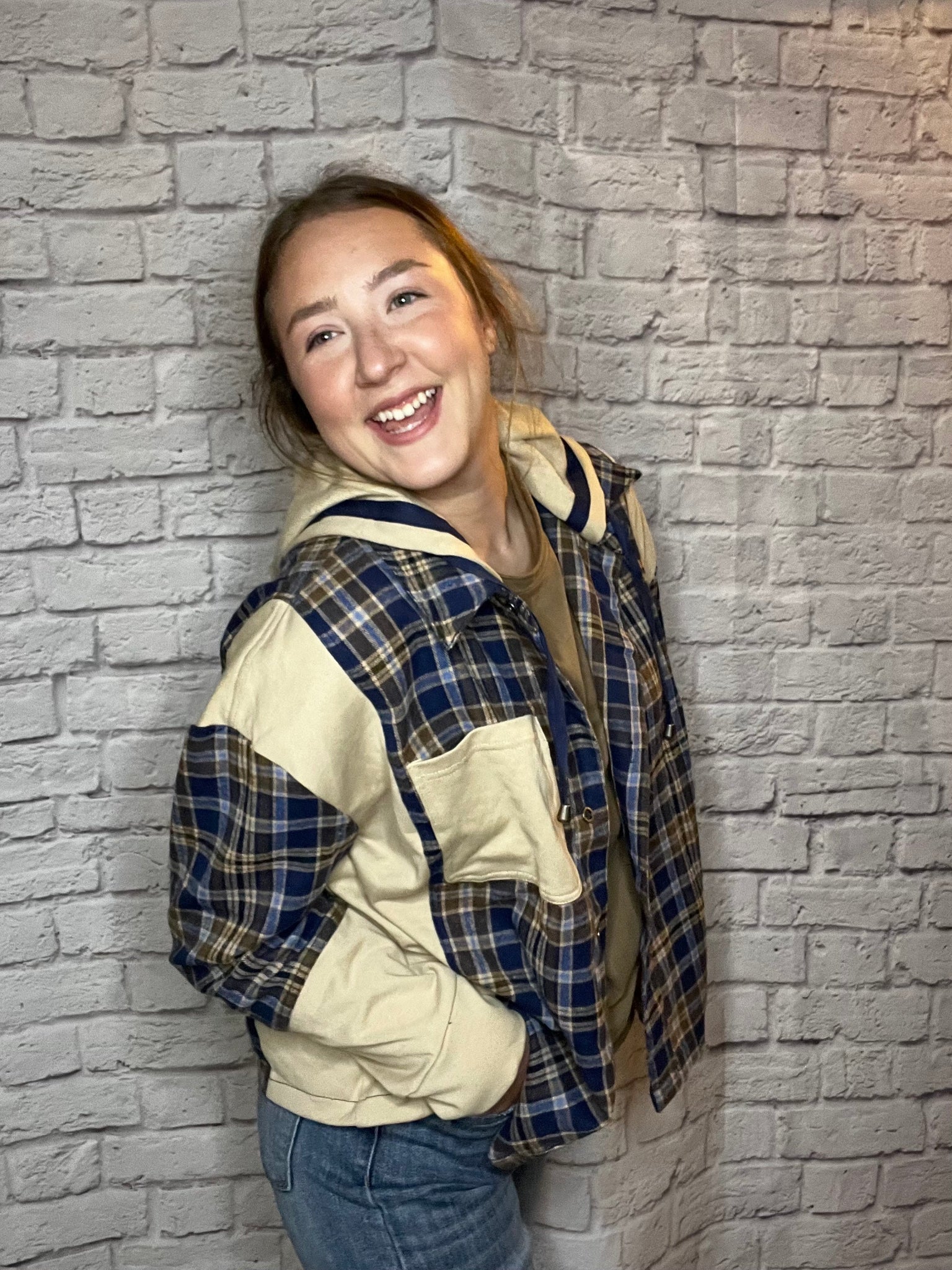 A woman wearing a blue, brown, and cream plaid shacket featuring cream contrast sleeves and large front pocket.