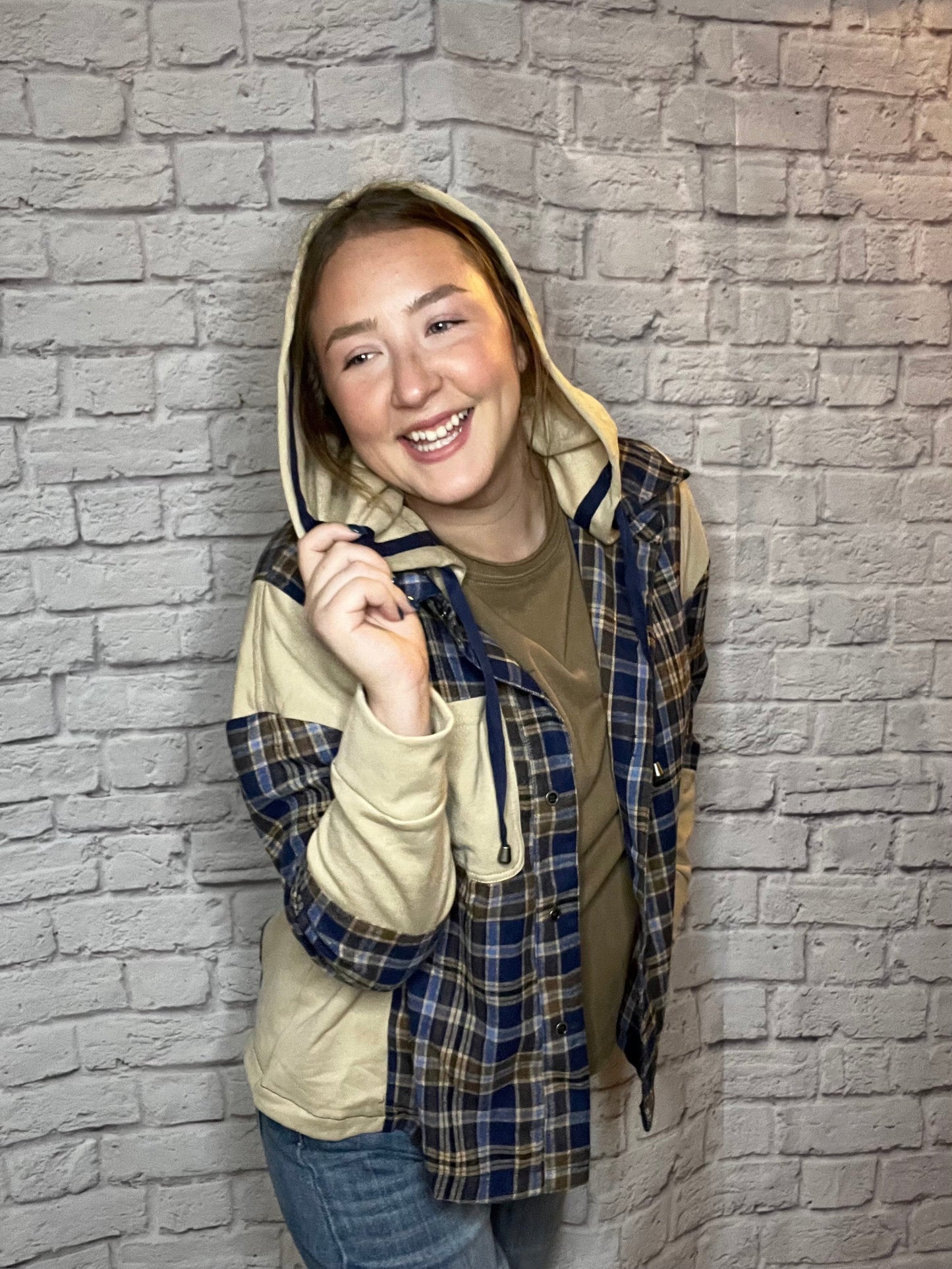 A woman wearing a blue, brown, and cream plaid shacket featuring cream contrast sleeves and large front pocket.