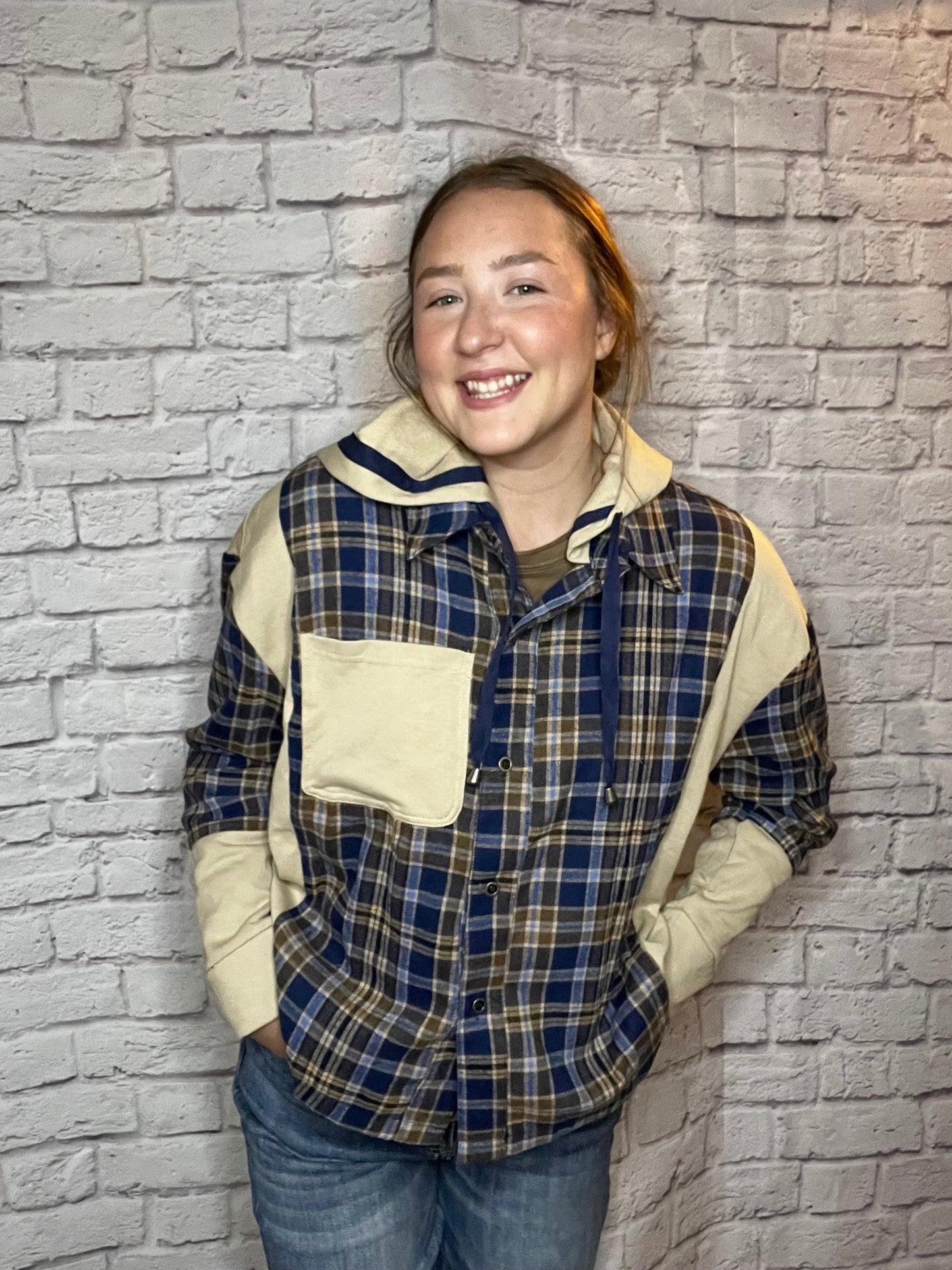 A woman wearing a blue, brown, and cream plaid shacket featuring cream contrast sleeves and large front pocket.