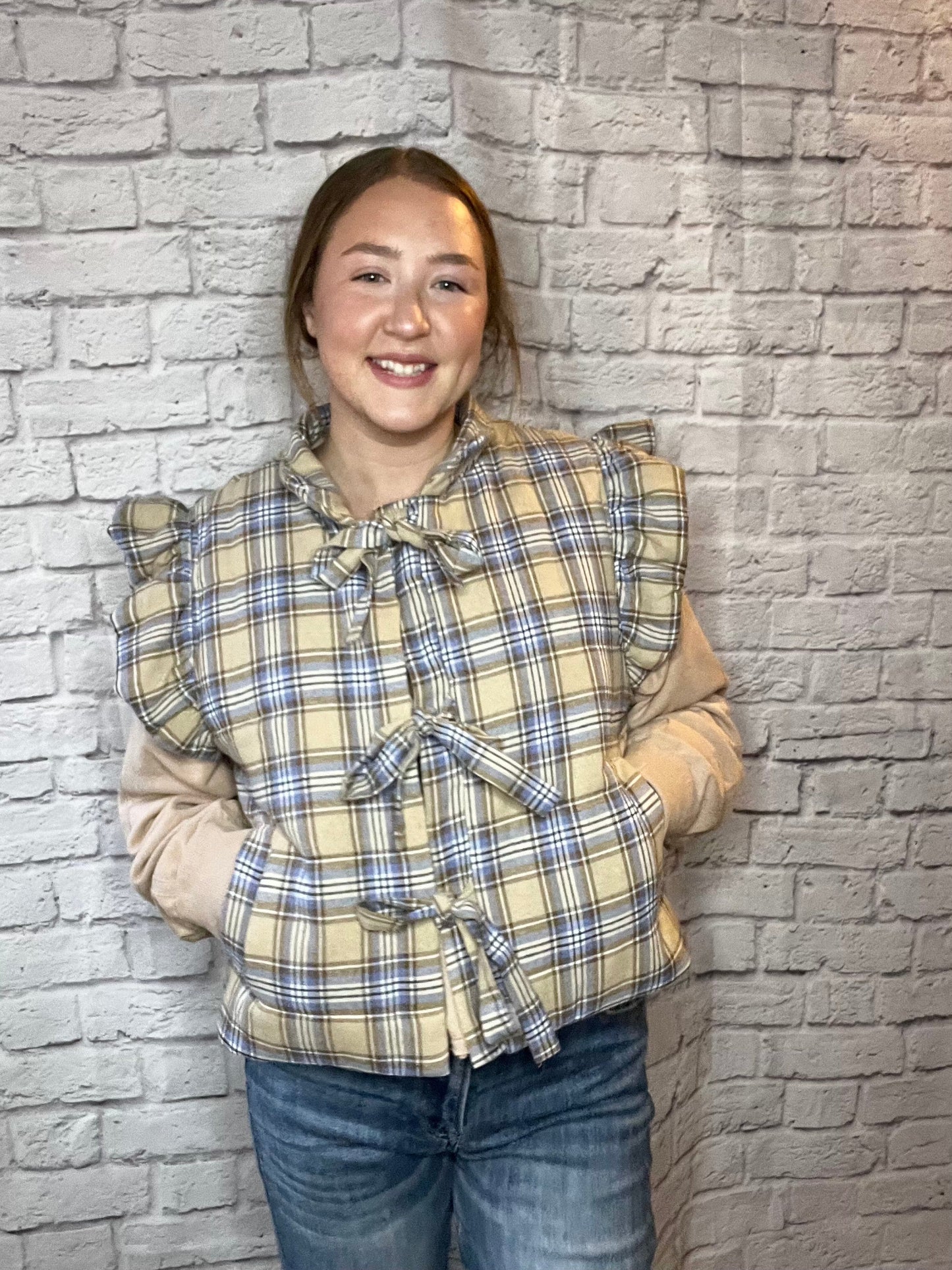 Cozy plaid puffer vest with ruffled shoulders and three front tie closures in beige, blue, and cream tones.
