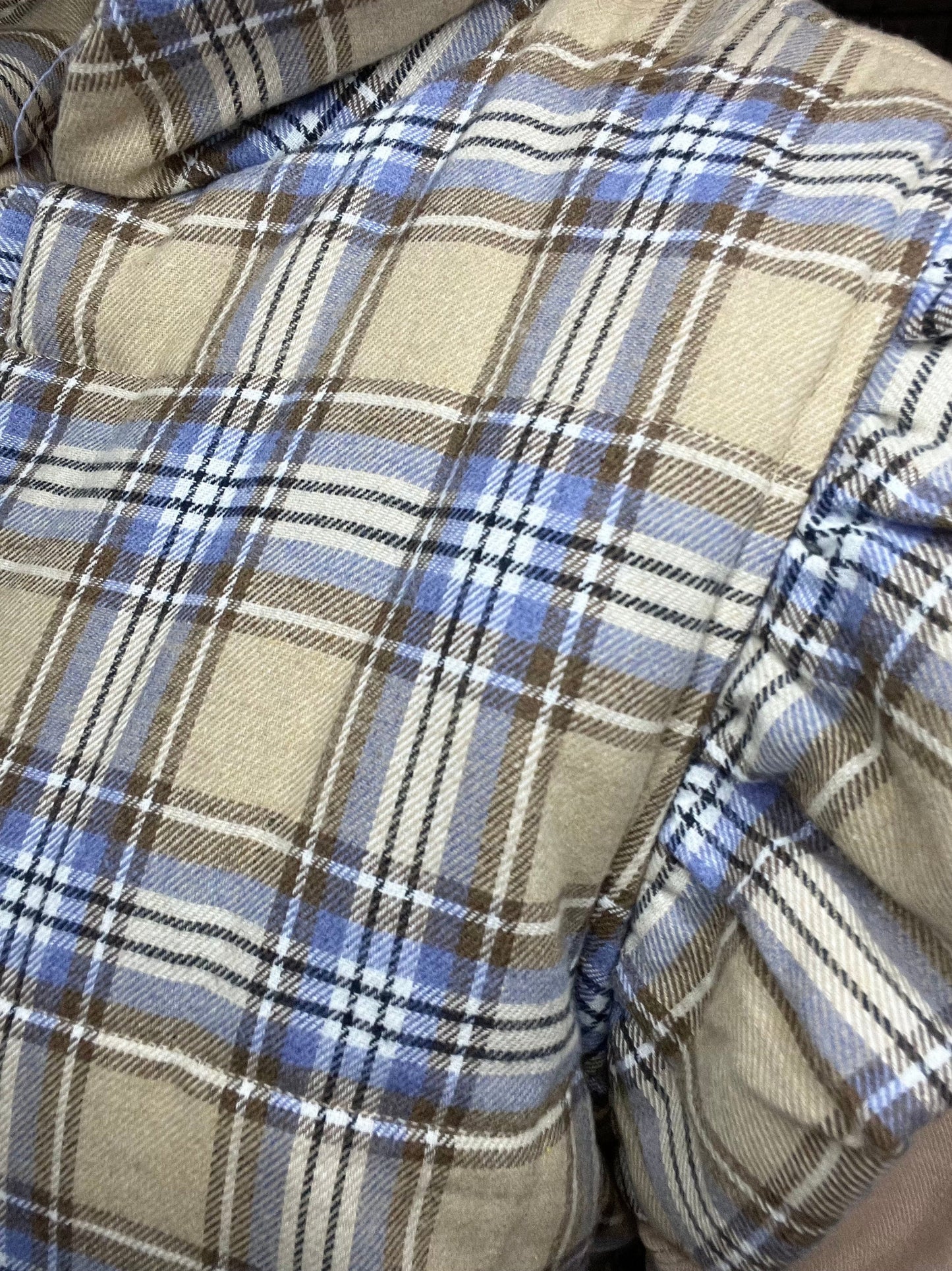 cozy plaid puffer vest with ruffled shoulders and three front tie closures in beige, blue, and cream tones.