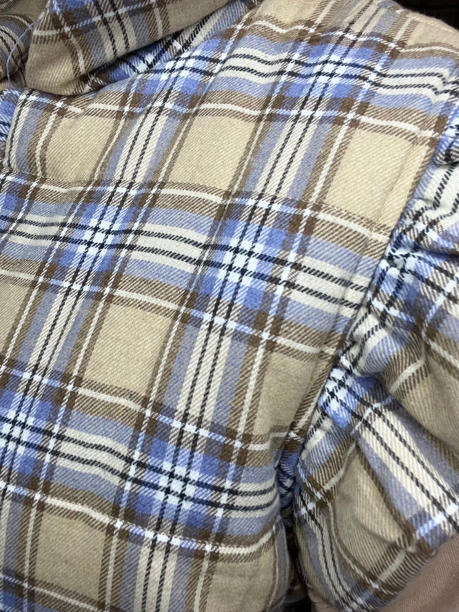 cozy plaid puffer vest with ruffled shoulders and three front tie closures in beige, blue, and cream tones.