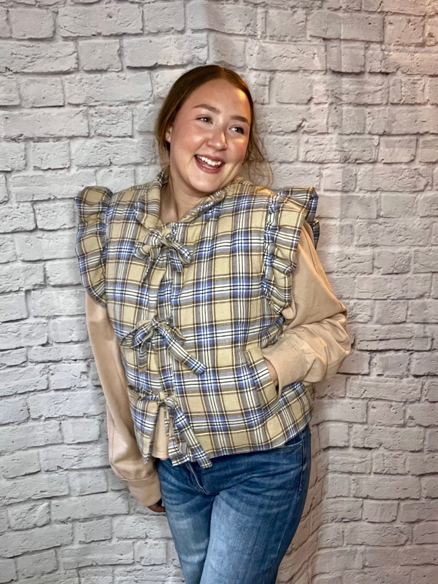cozy plaid puffer vest with ruffled shoulders and three front tie closures in beige, blue, and cream tones.