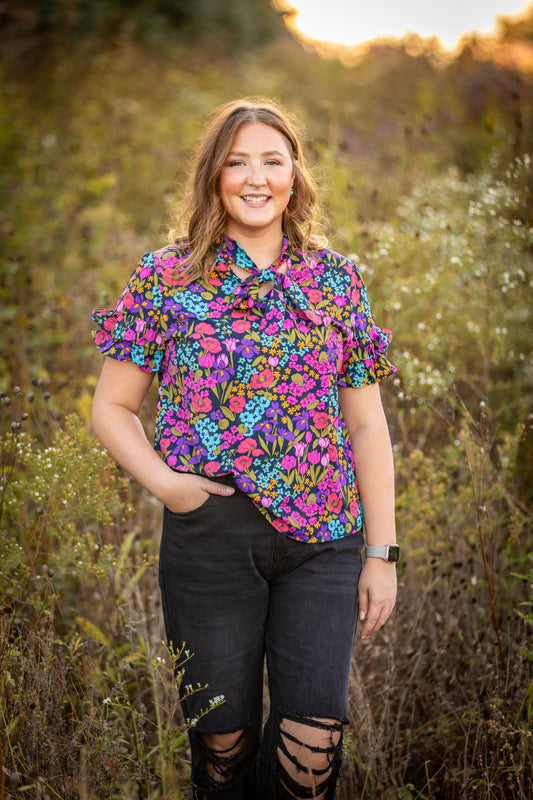 Women's purple floral blouse featuring a colorful floral print, classic collared neckline, and short sleeves.