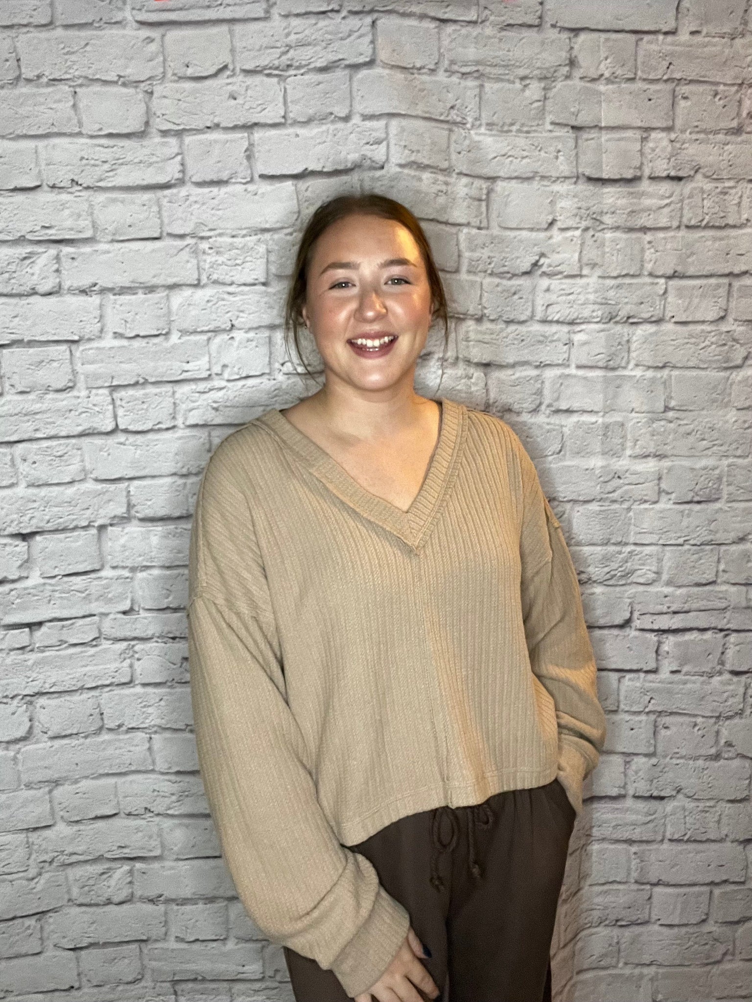 A woman wearing a relaxed fit, ribbed tan V-neck sweater.