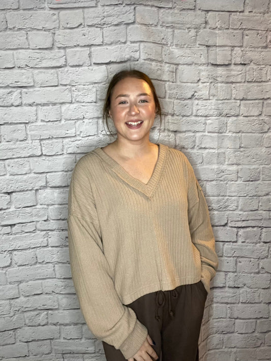 A woman wearing a relaxed fit, ribbed tan V-neck sweater.