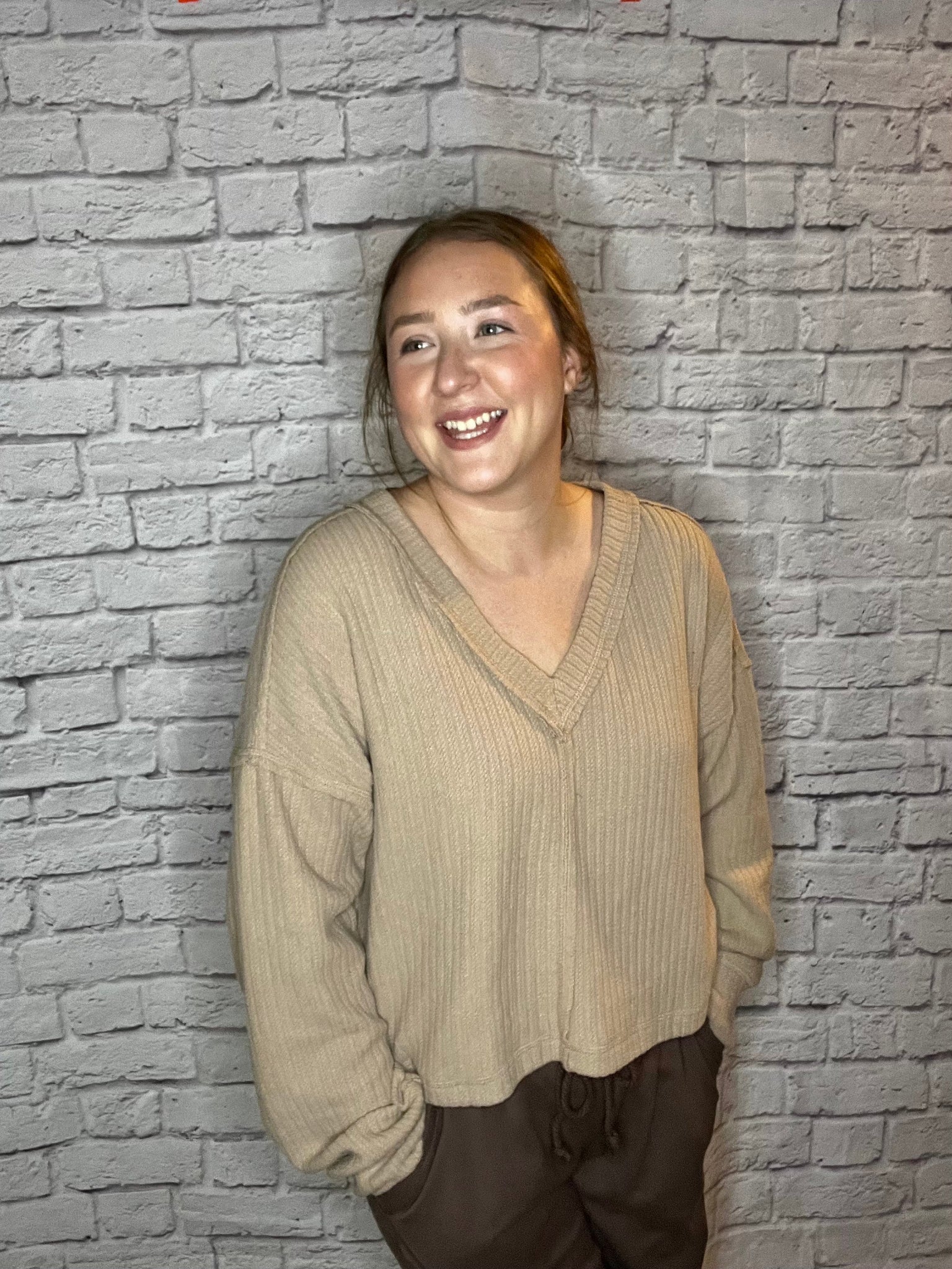 A woman wearing a relaxed fit, ribbed tan V-neck sweater.