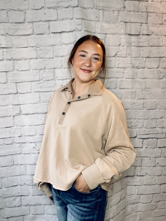 A woman wearing a soft tan pullover with a snap-button collar and relaxed fit.