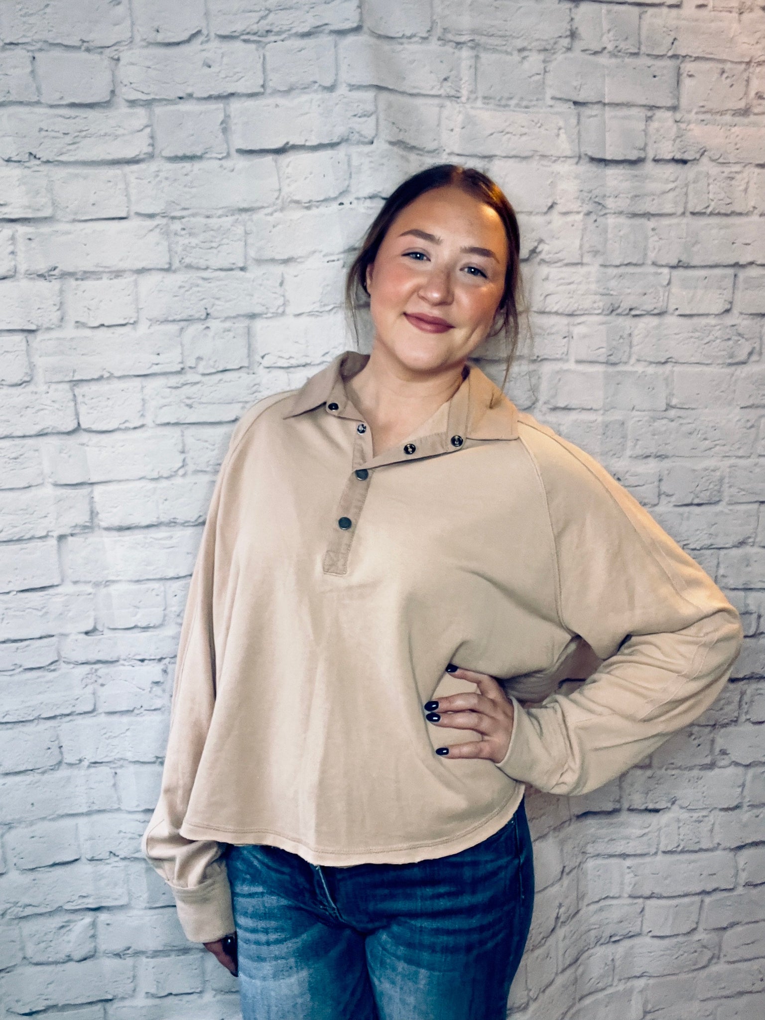 A woman wearing a soft tan pullover with a snap-button collar and relaxed fit.