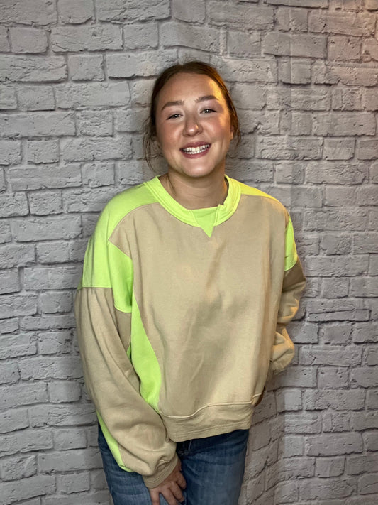 A woman wearing a casual sweatshirt with tan and neon yellow color-block sleeves and accents.