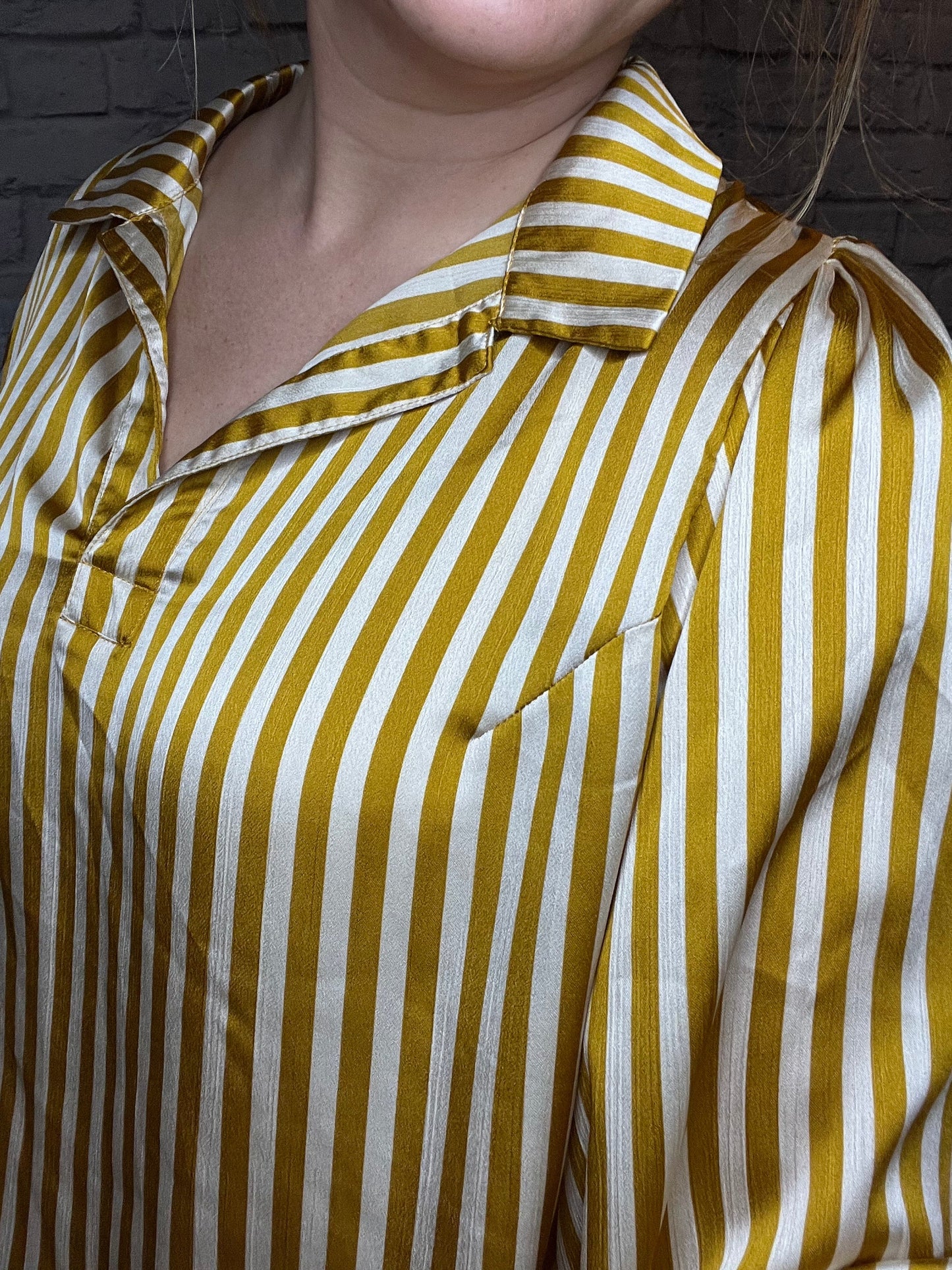 A woman wearing a mustard yellow and white vertical striped blouse with a relaxed fit, collared neckline, and gathered sleeves.