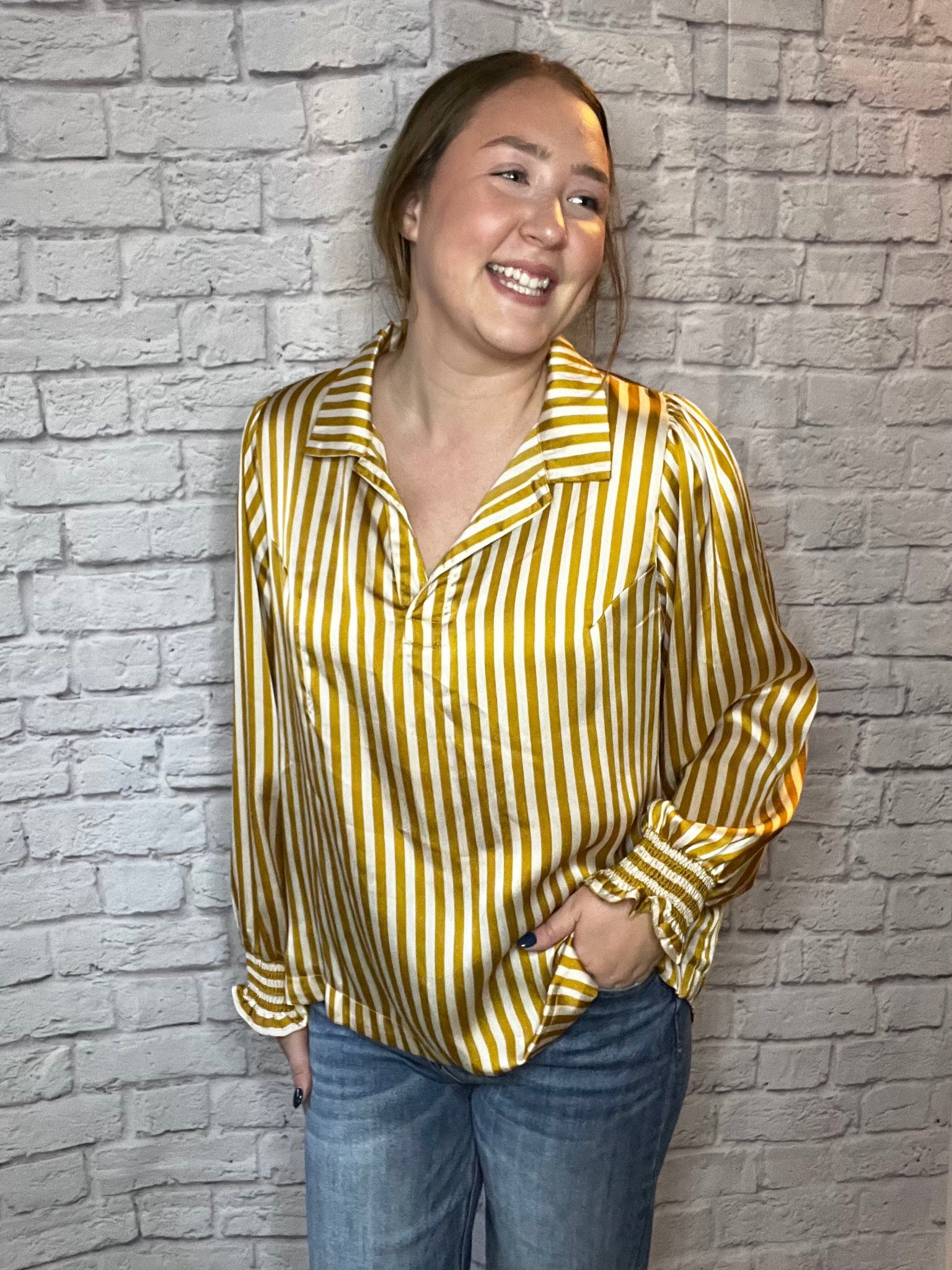 A woman wearing a mustard yellow and white vertical striped blouse with a relaxed fit, collared neckline, and gathered sleeves.