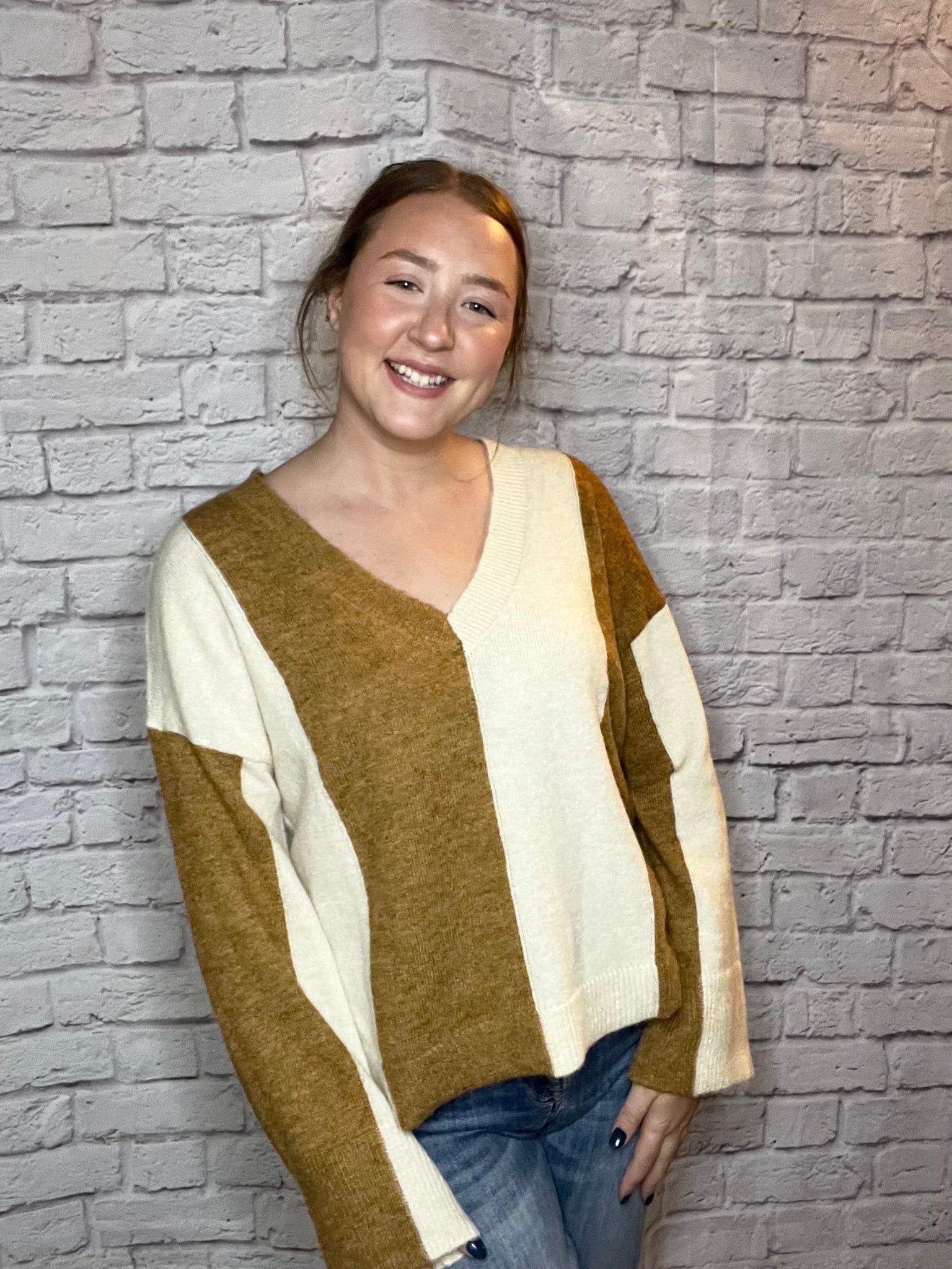 A woman wearing a soft color-block V-neck sweater featuring warm brown and cream panels.
