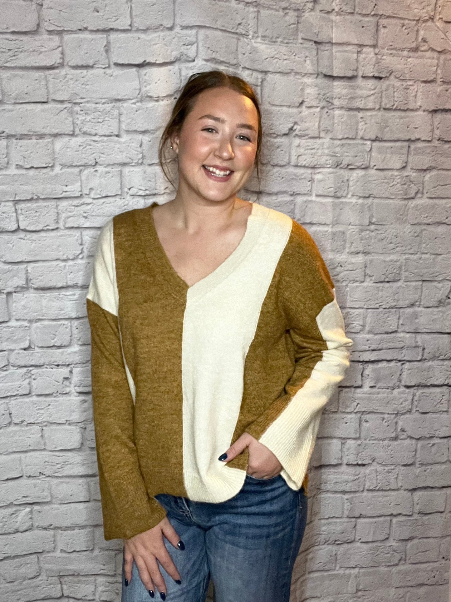 A woman wearing a soft color-block V-neck sweater featuring warm brown and cream panels.
