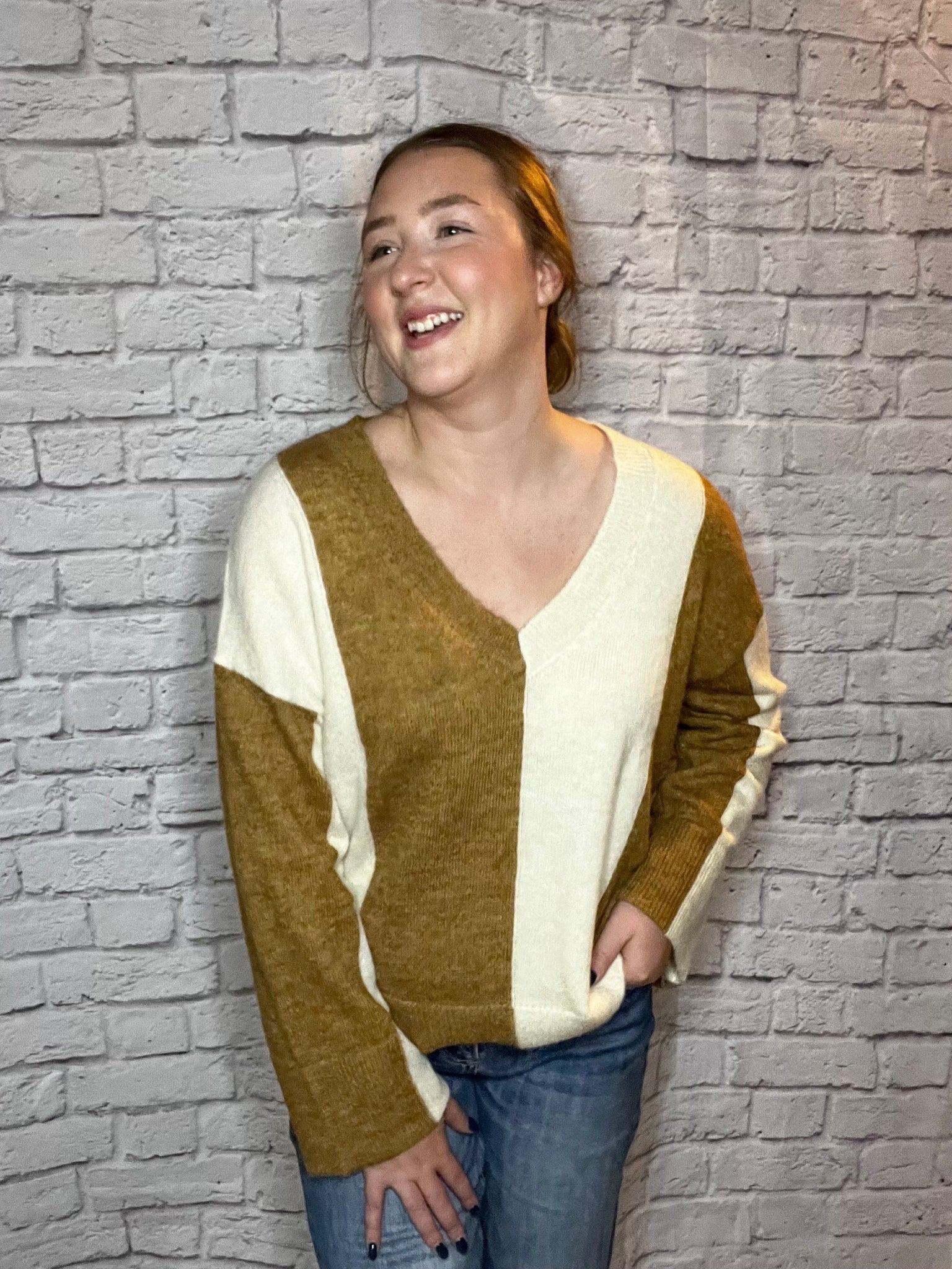 A woman wearing a soft color-block V-neck sweater featuring warm brown and cream panels.